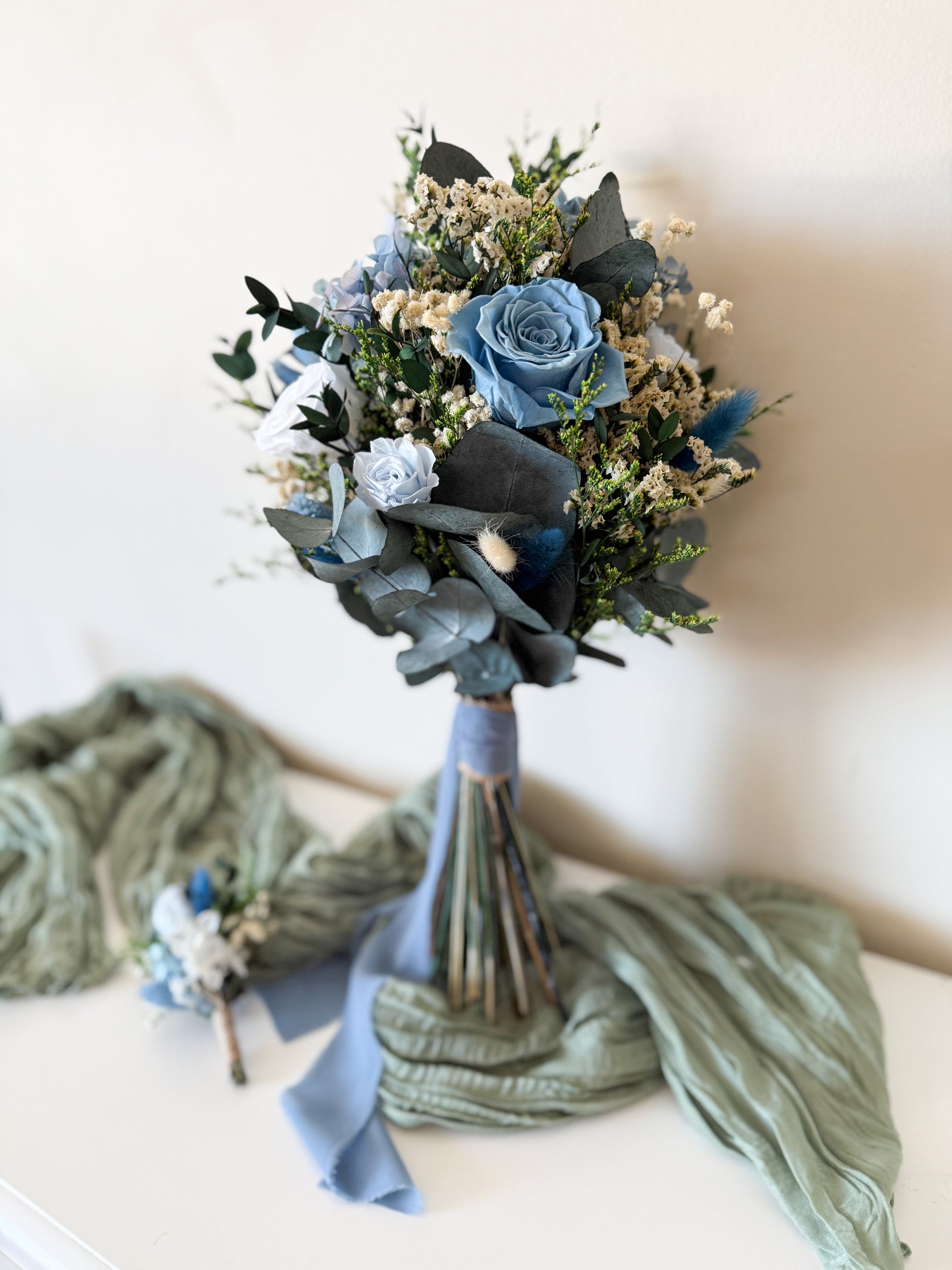 Handmade wedding bouquet in dusty blue and ivory tones with preserved greenery and sola wood flowers, ideal for brides.