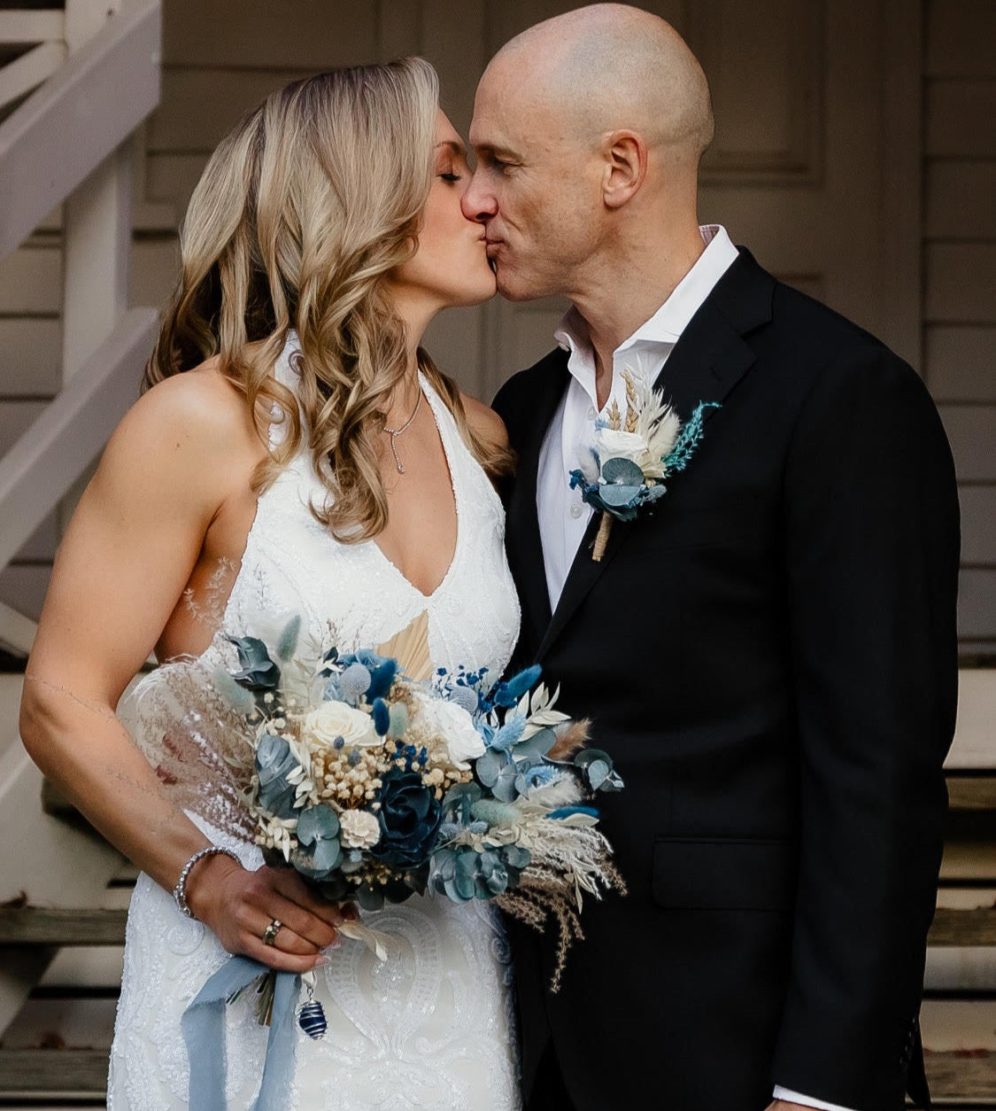 Couple kissing outdoors with a wedding flowers in dusty blue colours