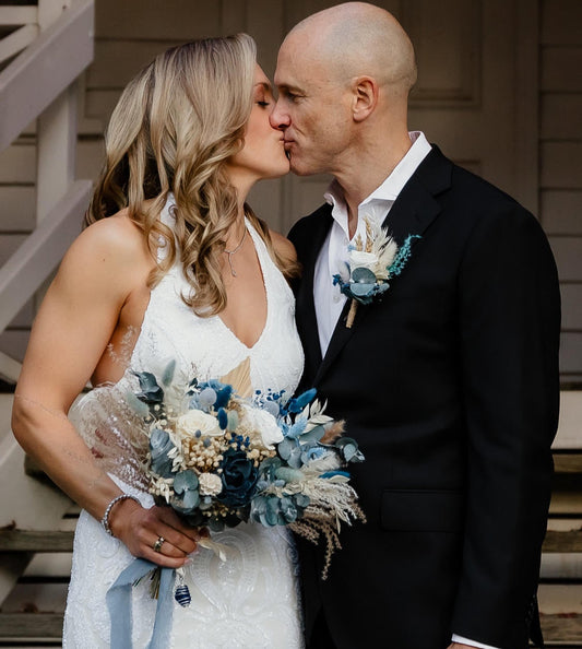 Couple kissing outdoors with a wedding flowers in dusty blue colours