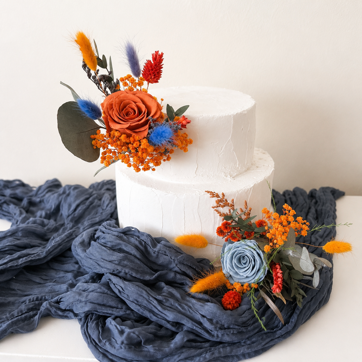 Elegant wedding cake styling with dusty blue roses, amber blooms and autumn foliage in a rustic, modern botanical palette.