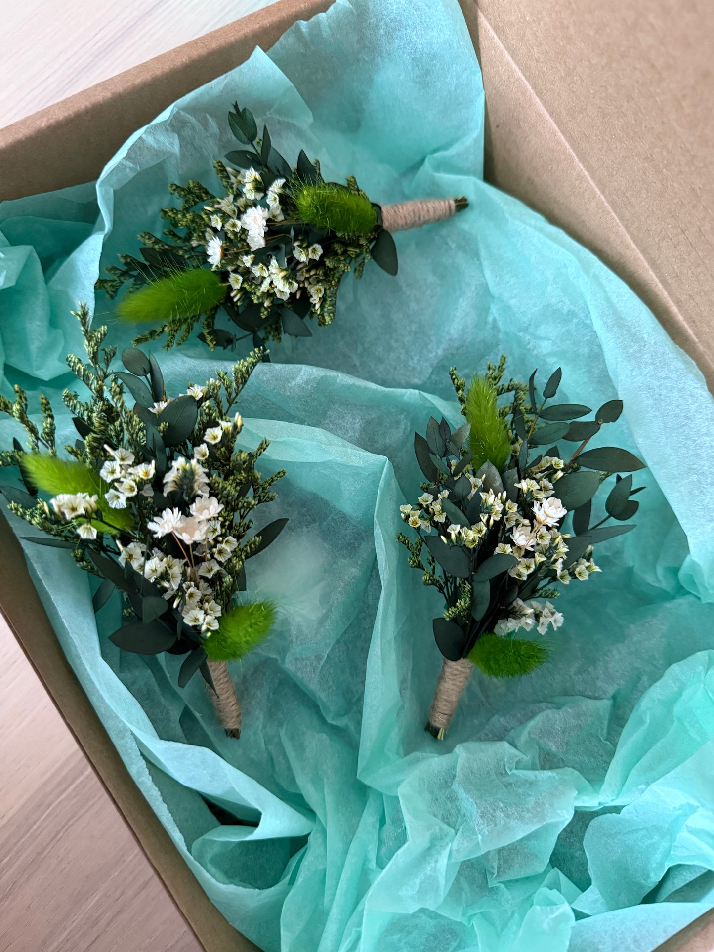 Three small floral arrangements on light blue tissue paper inside a cardboard box.