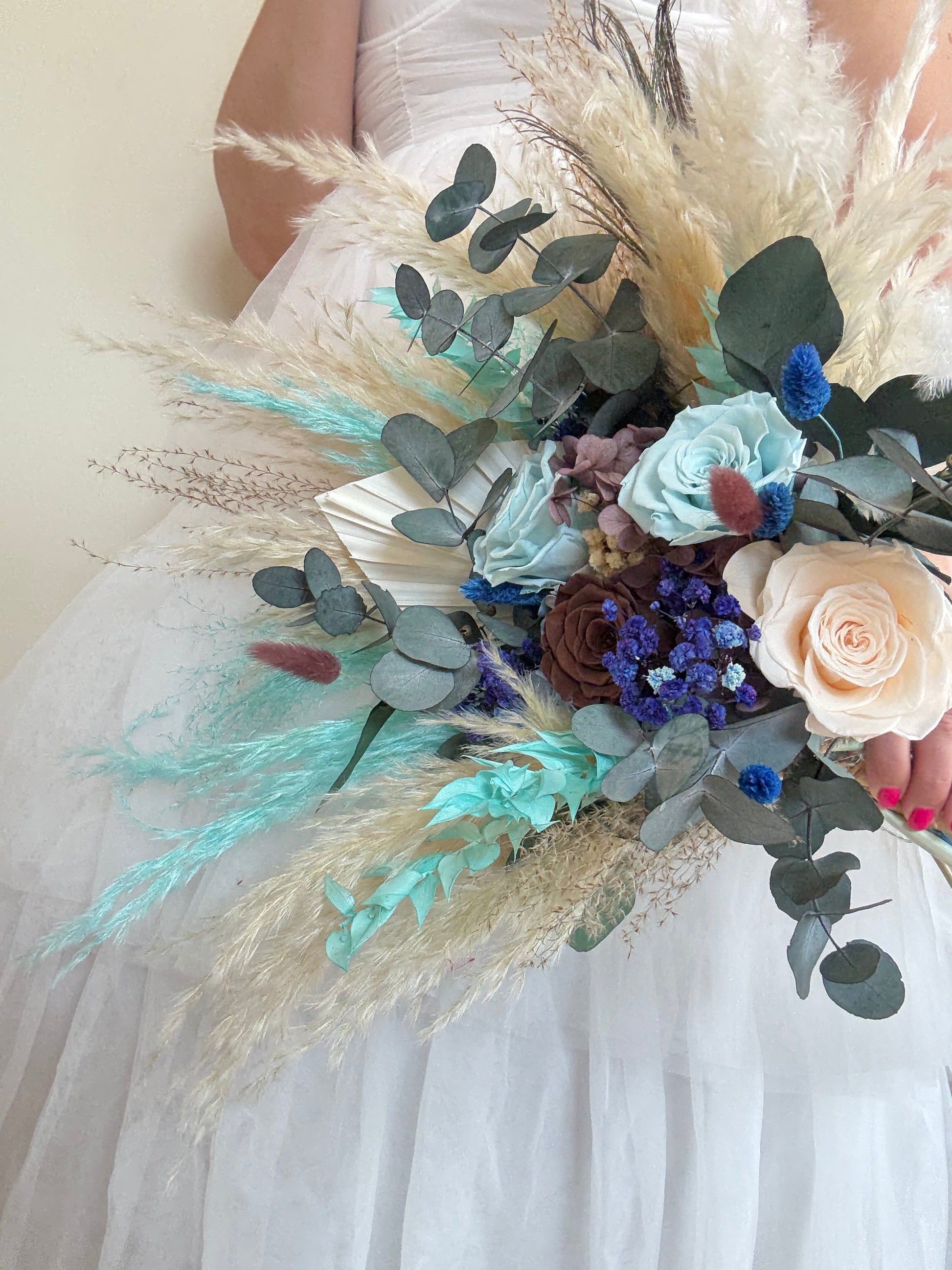 Flat lay of teal and navy blue dried bouquet with white silk ribbon and sage green fabric.