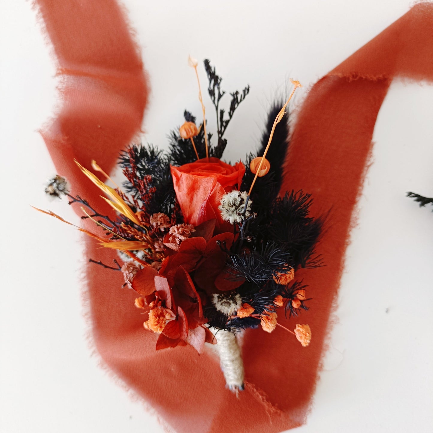unique dried floral groom pin with navy preserved leaves, orange blooms, and natural elements