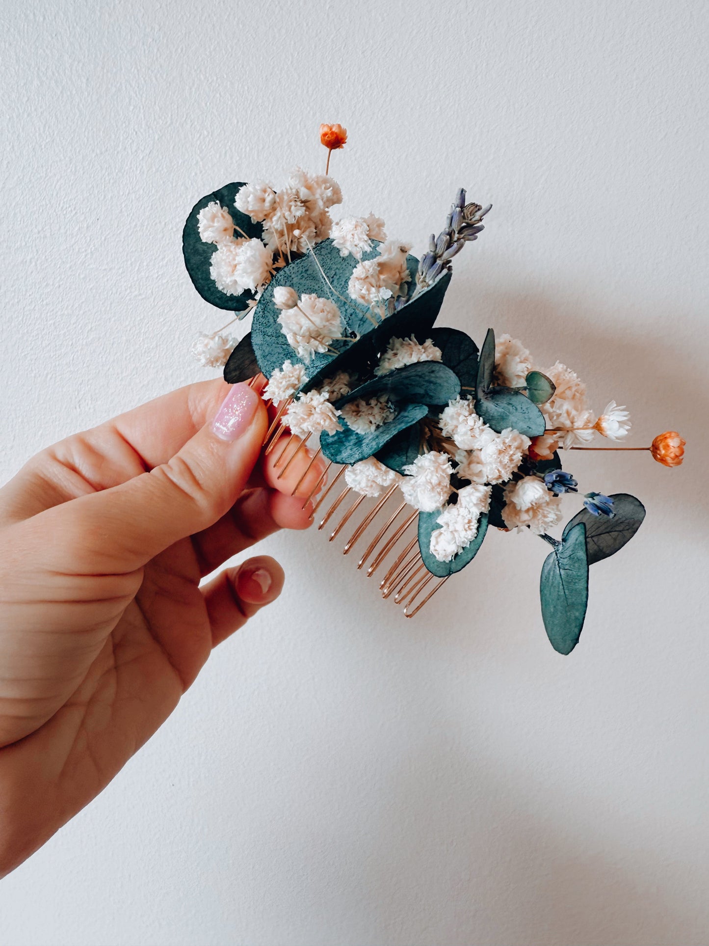 Hair comb with floral and leaf decorations held by a hand against a plain background