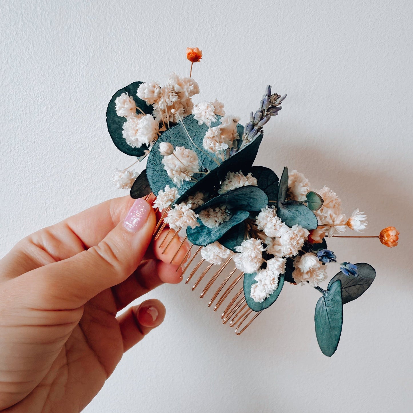Hair comb with floral and leaf decorations held by a hand against a plain background