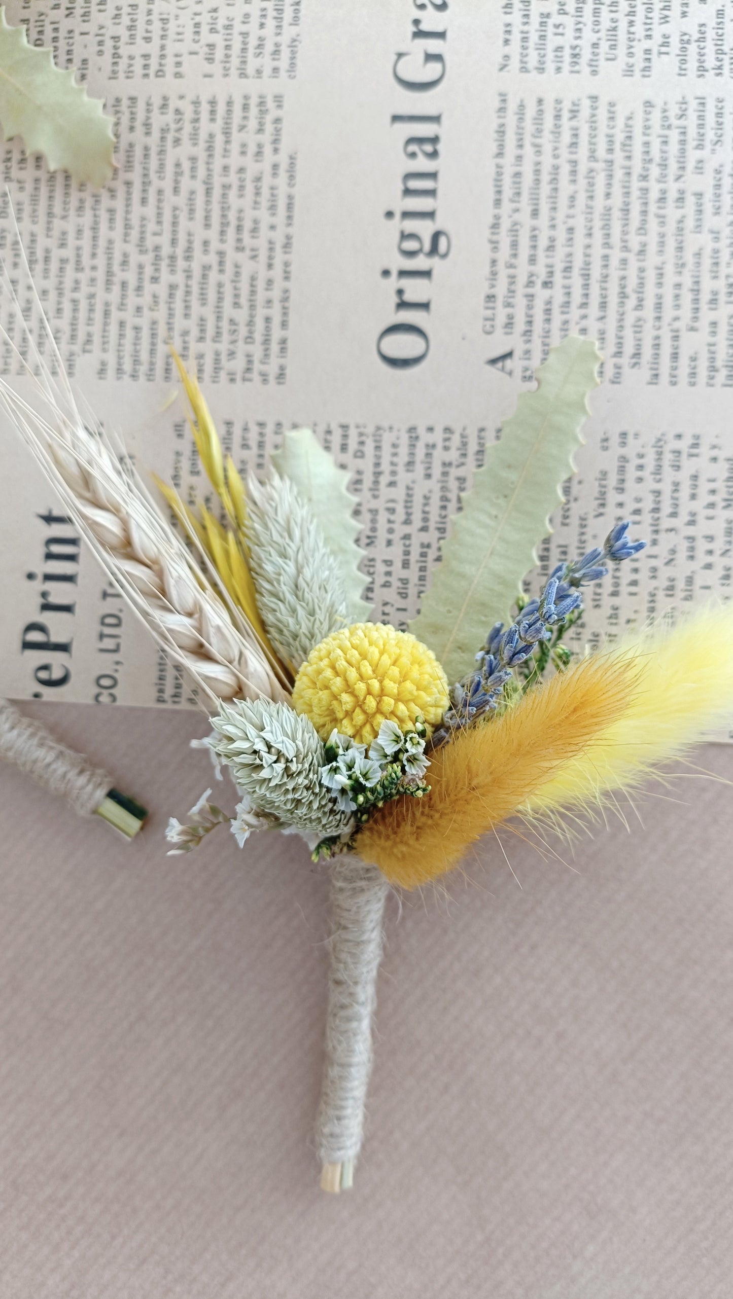 handcrafted boutonnières featuring yellow billy buttons, fluffy bunny tails, dried lavender, and greenery – styled on vintage newspaper background.