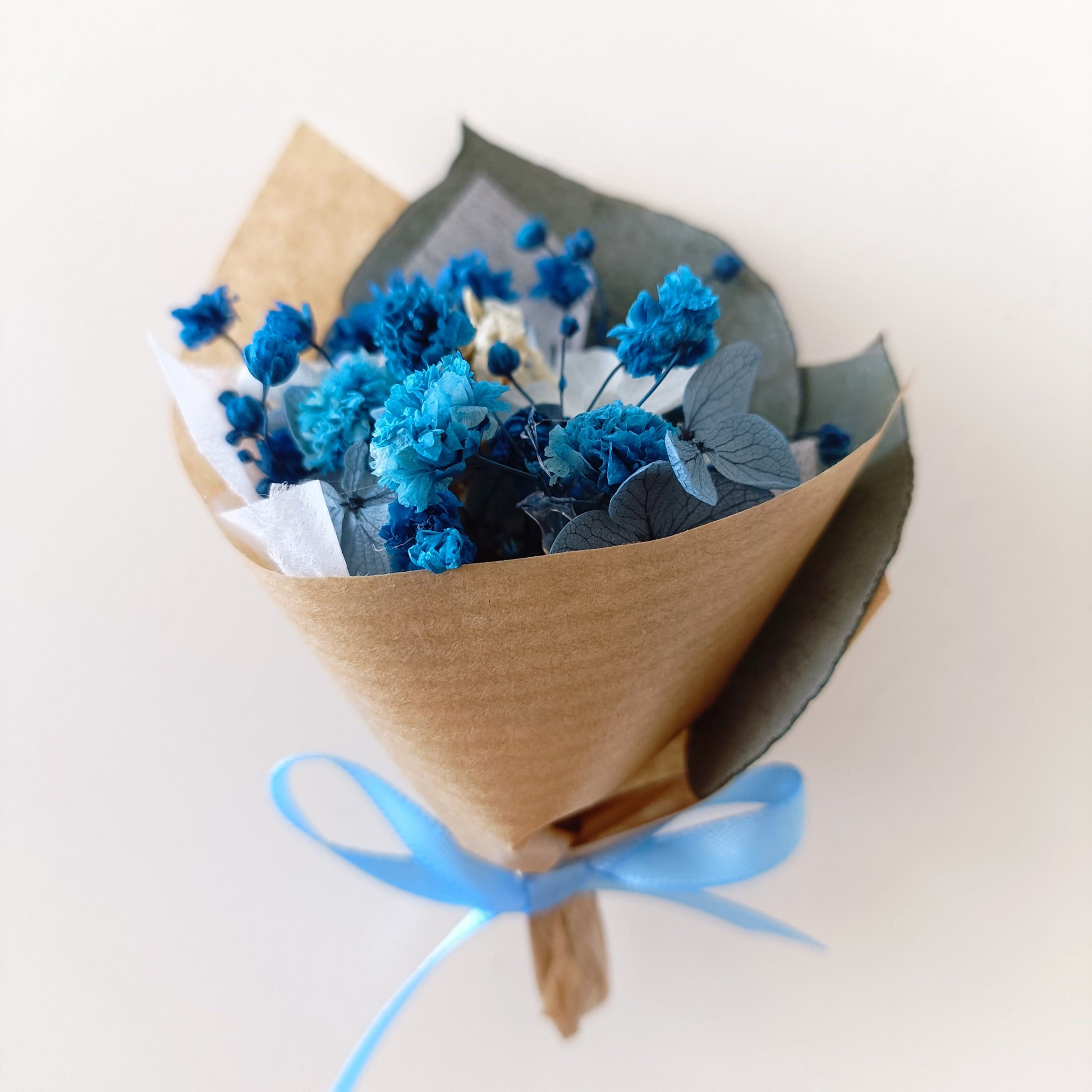 Petite kraft-wrapped dried flower posies in blue and white, with preserved blooms and natural textures. Rustic and modern favour idea.