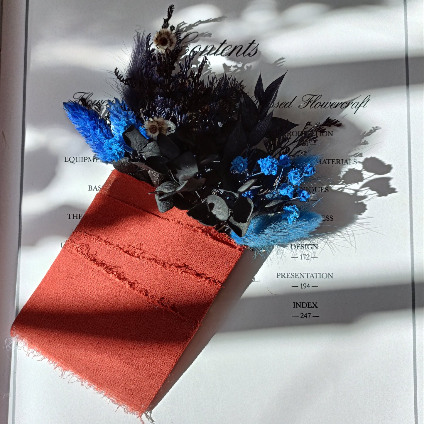 Bold boho groom boutonniere with dried florals in dark blue, black foliage and rustic burnt orange wrap