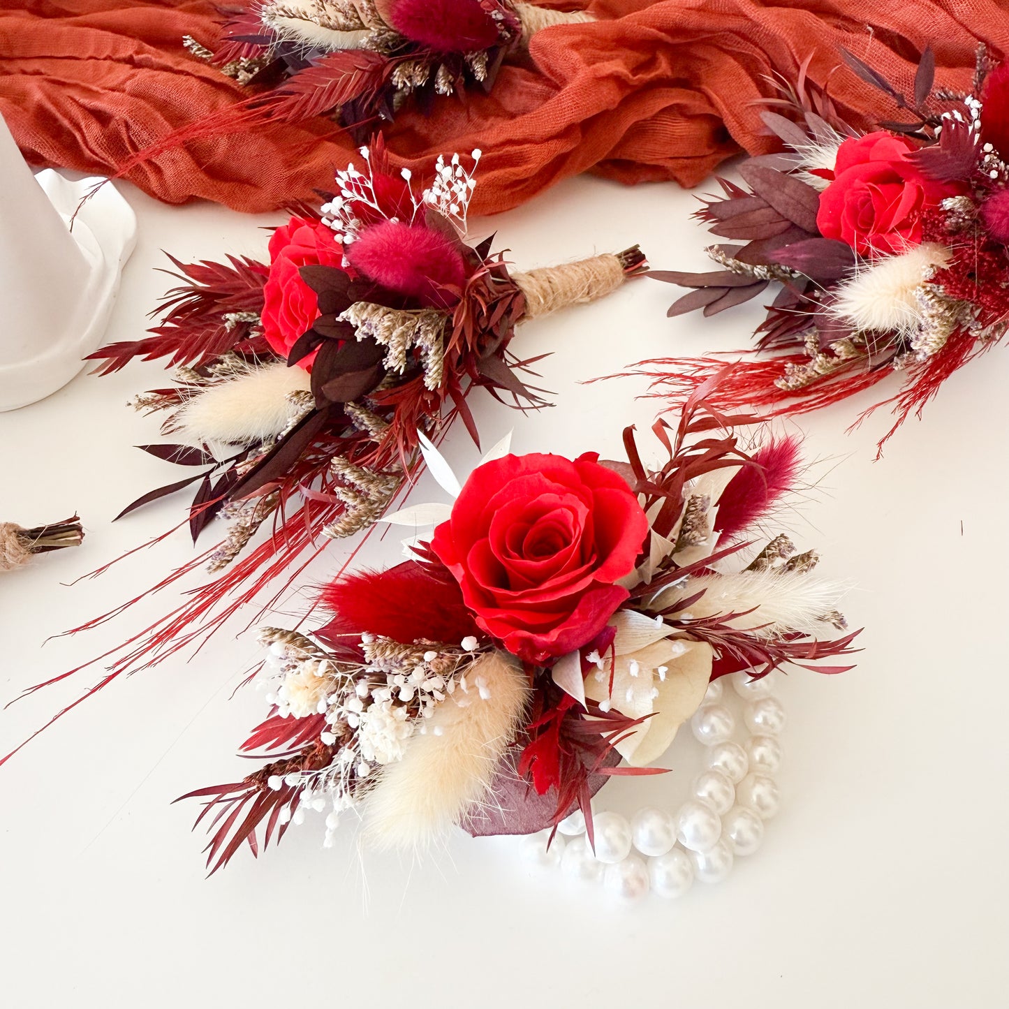 Decorative floral boutonniere and corsage with red roses and feathers on a white surface