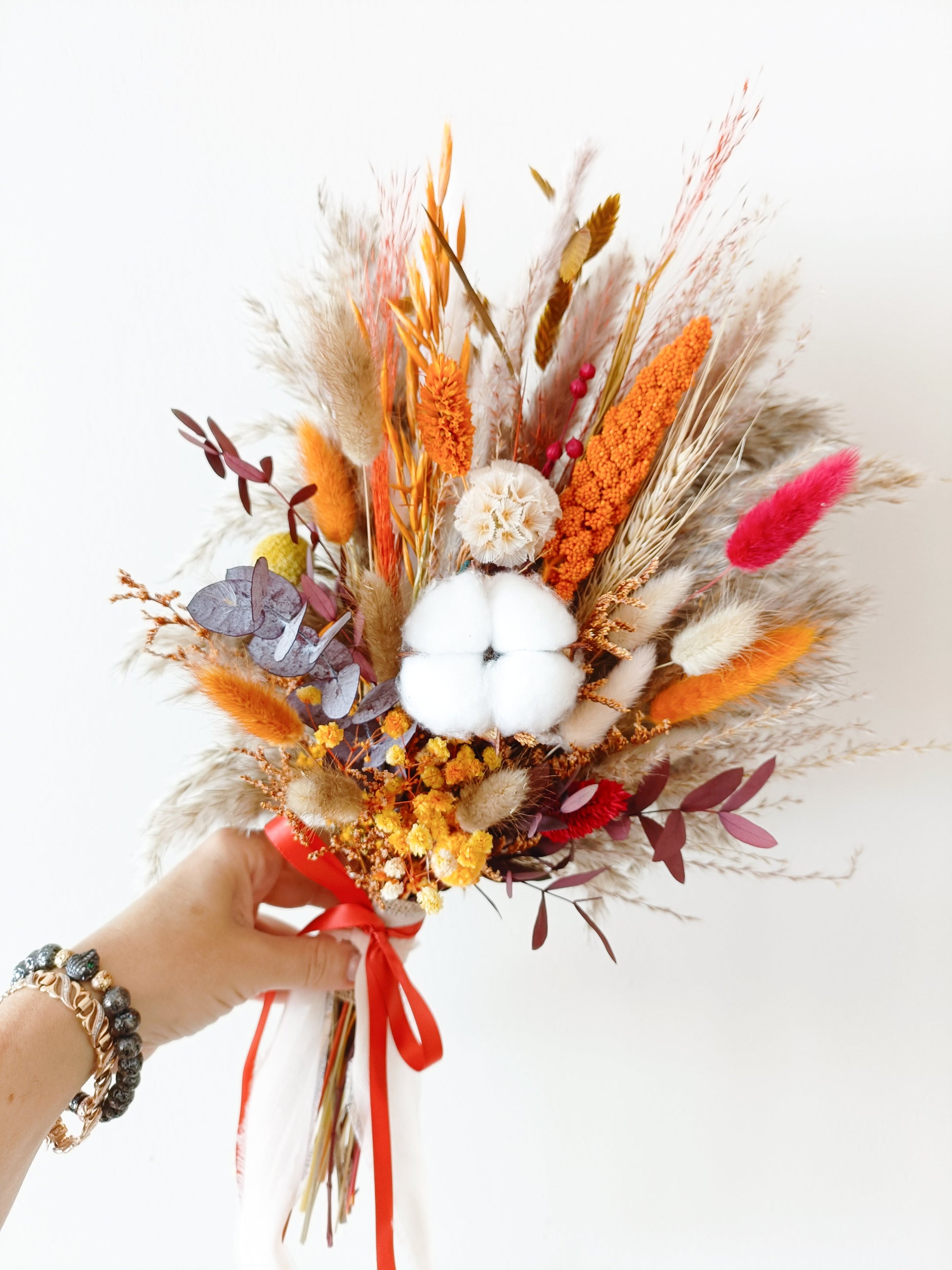 Boho wedding bouquet with preserved flowers, cotton, and burnt orange tones, held in hand.