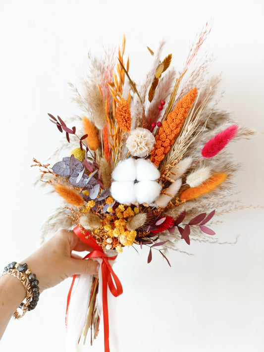 Boho wedding bouquet with preserved flowers, cotton, and burnt orange tones, held in hand.