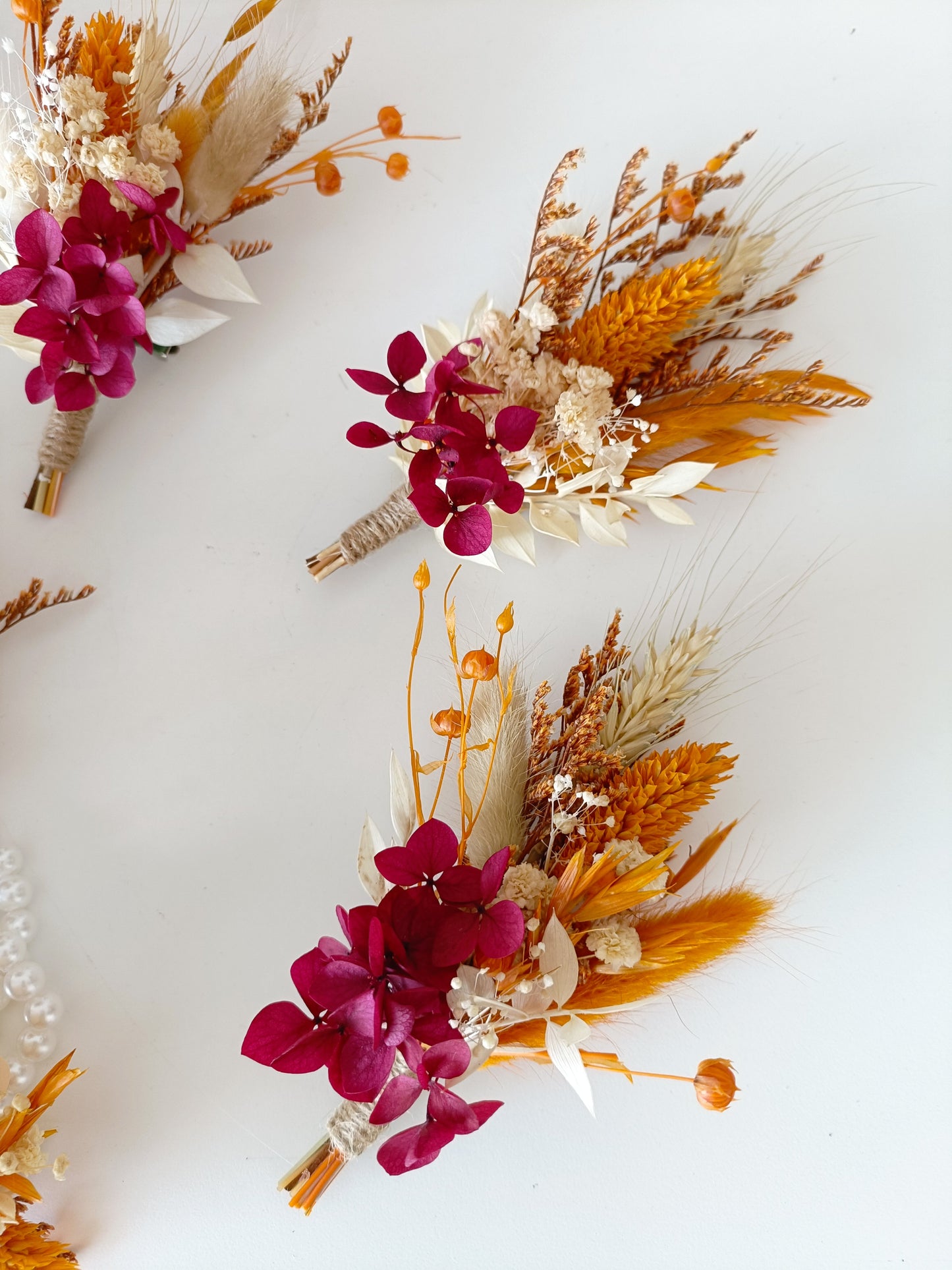 Groomsman boutonniere with vibrant pink, orange, and white preserved flowers on white background.