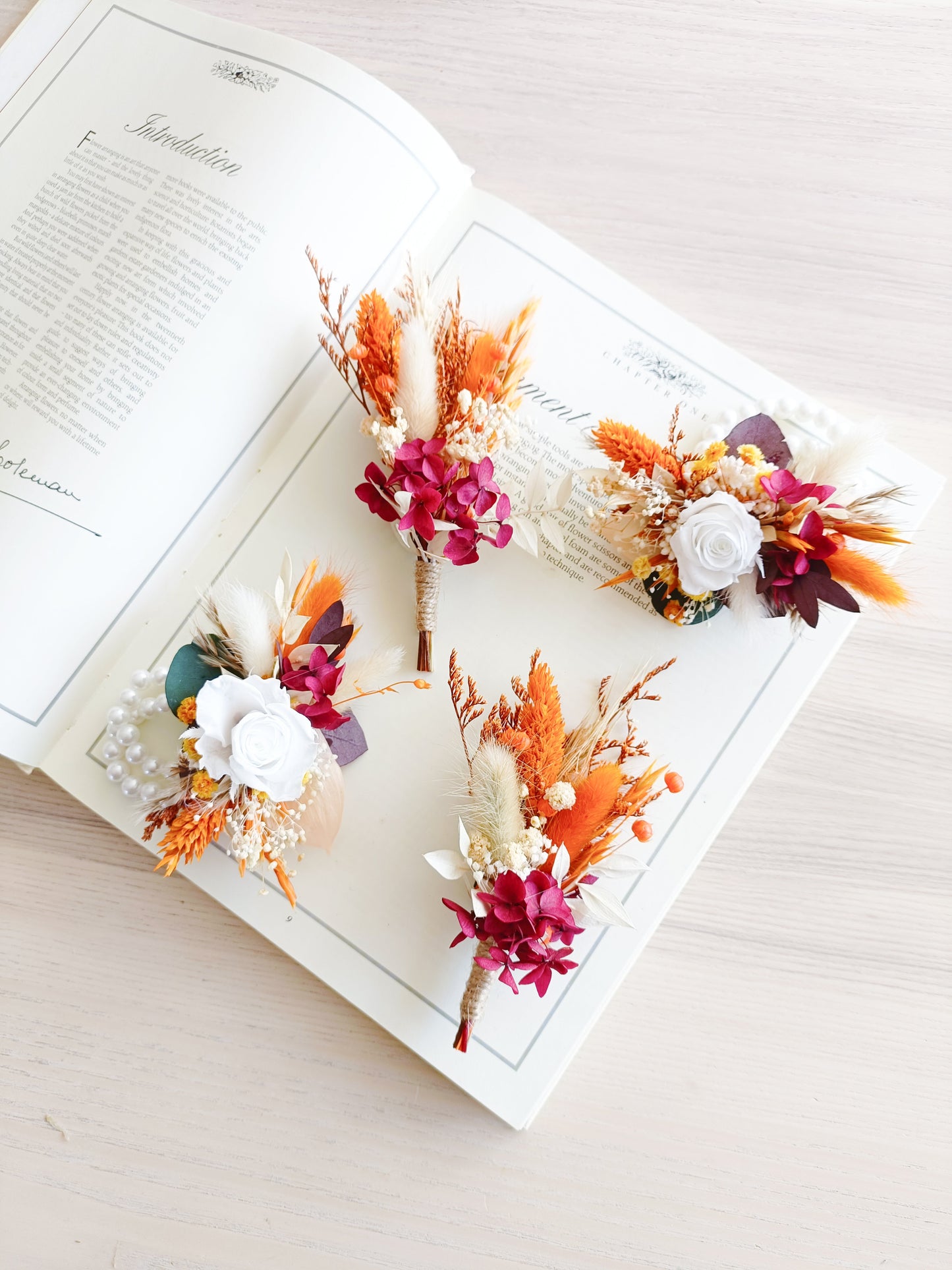 Flatlay of wedding boutonnieres and corsages in autumn-inspired colors of burgundy, orange, and white