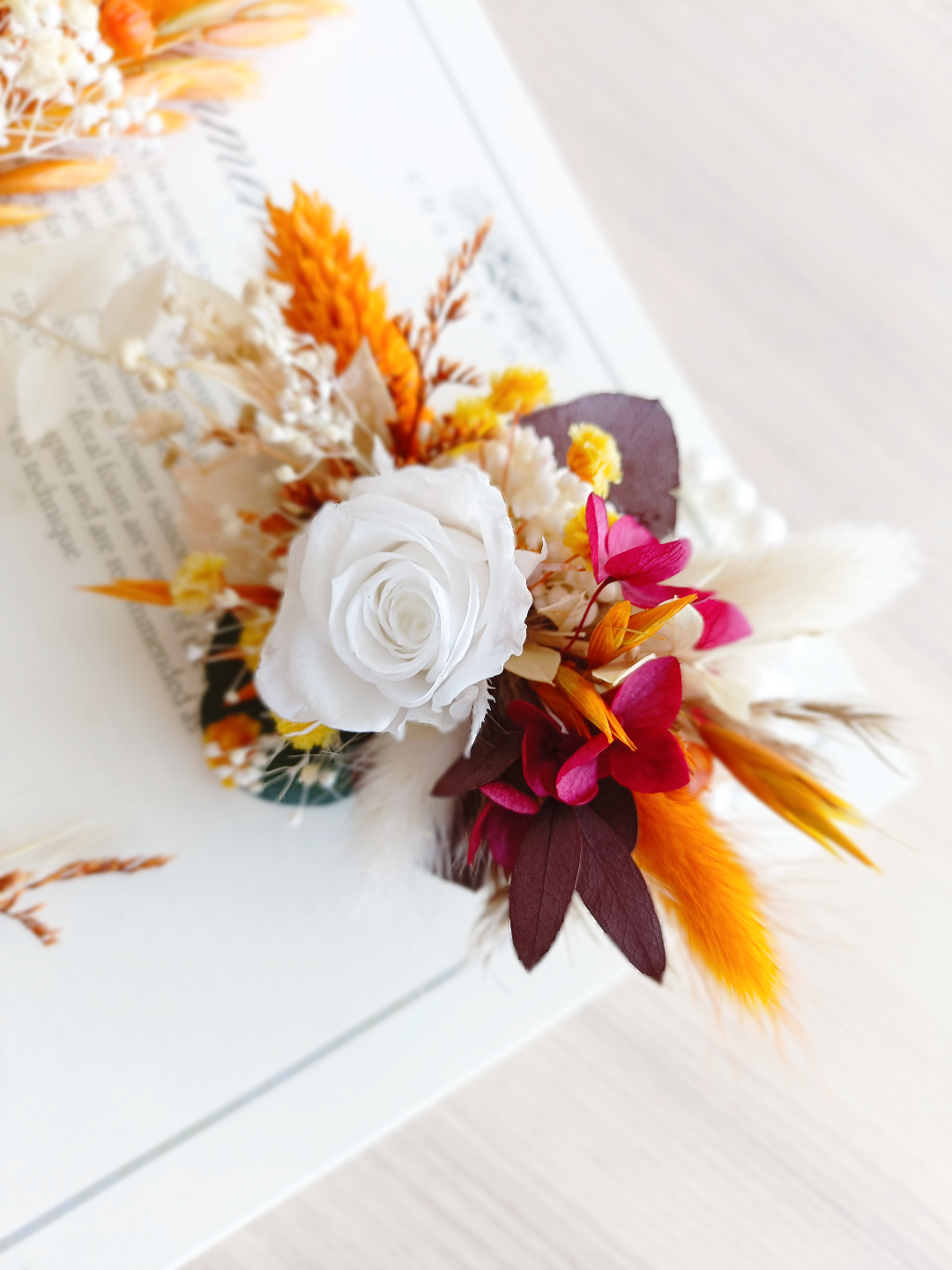 Wrist corsage with white preserved rose, orange accents, and burgundy dried flowers, worn on a hand.