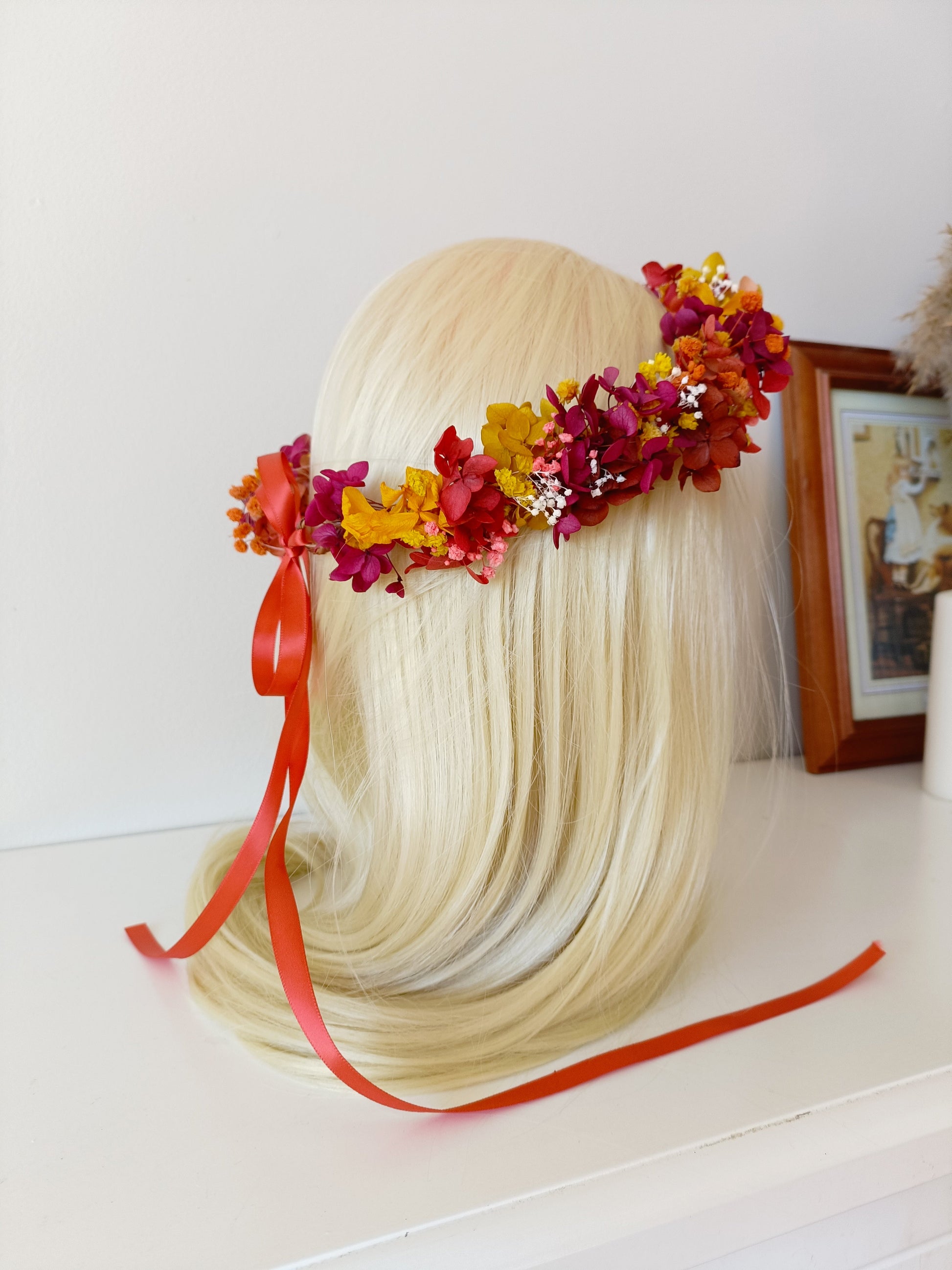 Bridal flower crown made of dried blooms in burgundy, orange, and yellow, displayed on a mannequin head.