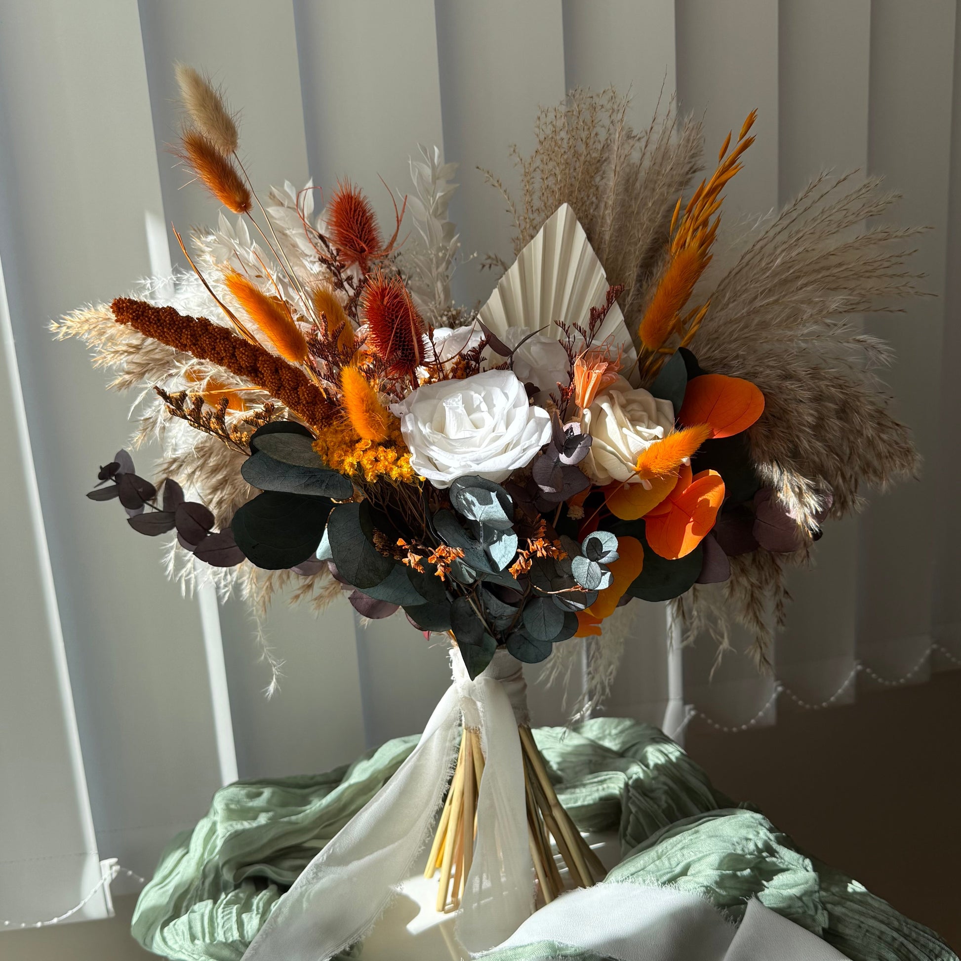 Rustic bridal bouquet featuring pampas grass, dried foliage, sola wood flowers, and bright terracotta accents — handmade boho bouquet for weddings.