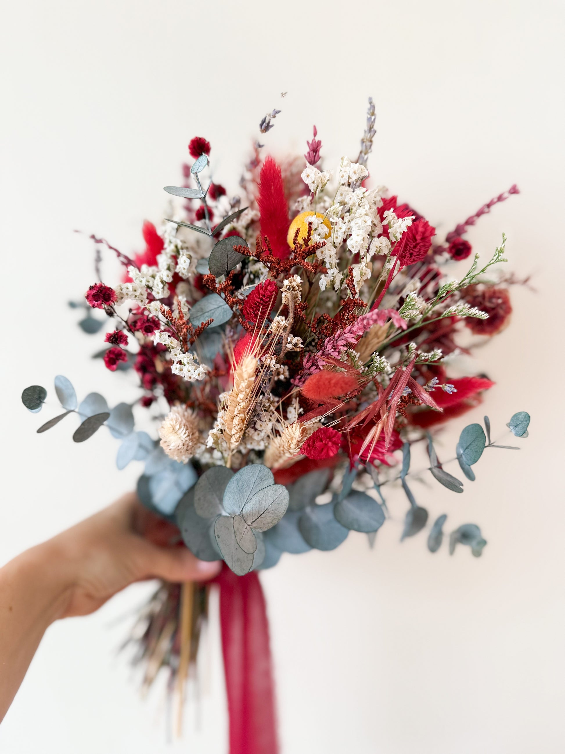 Rustic dried flower bridal bouquet tied with deep red ribbon on wooden table backdrop