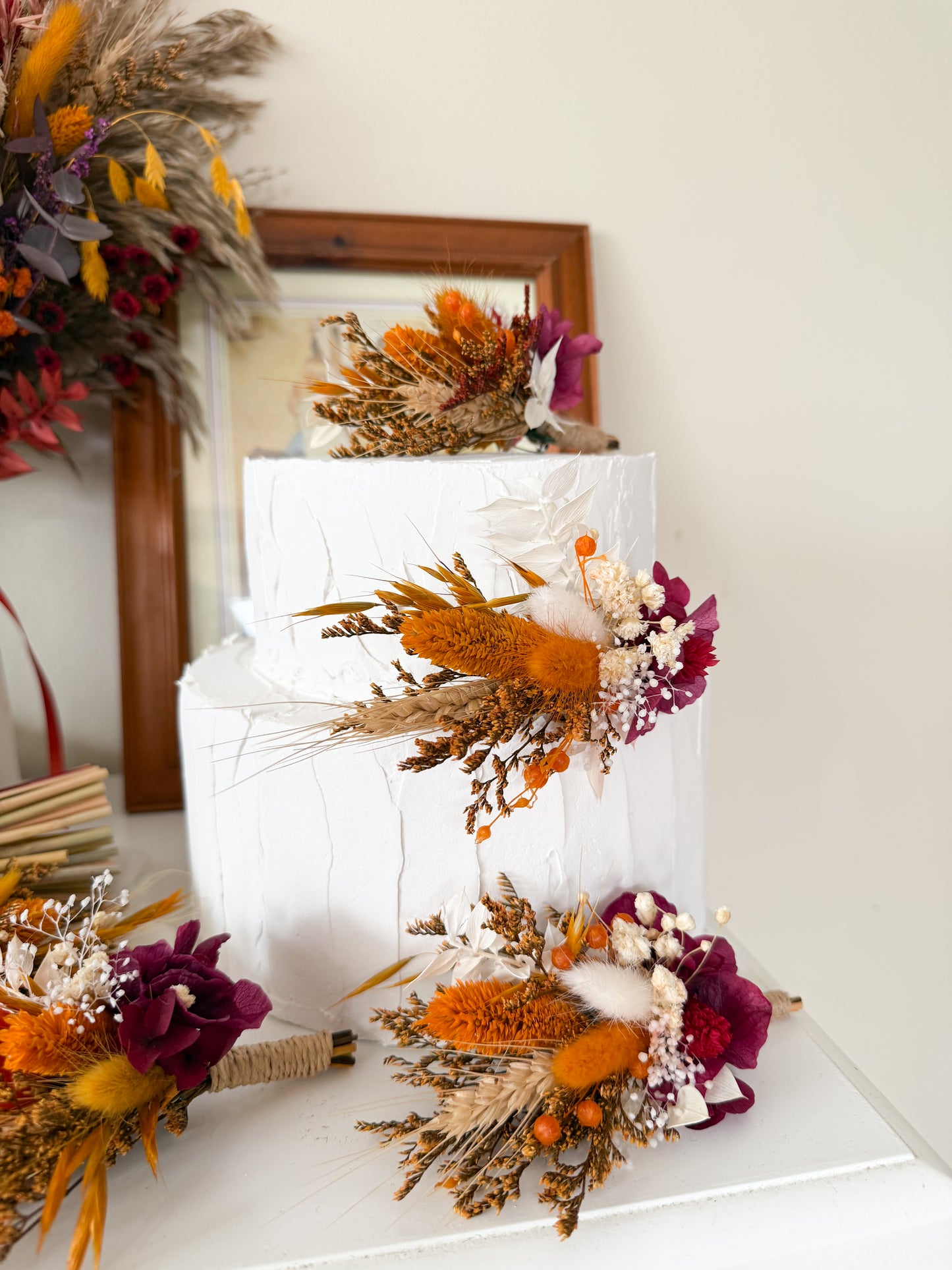 Boho style cake topper set made from dried flowers – pampas, cotton, terracotta, burgundy, rustic autumn wedding cake decoration. Decorative cake with autumnal flowers and wheat on a white surface.