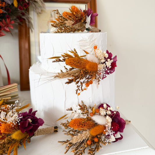 Handmade wedding cake floral decorations in rustic terracotta tones, arranged with terracotta grasses, burgundy accents and natural dried botanicals.