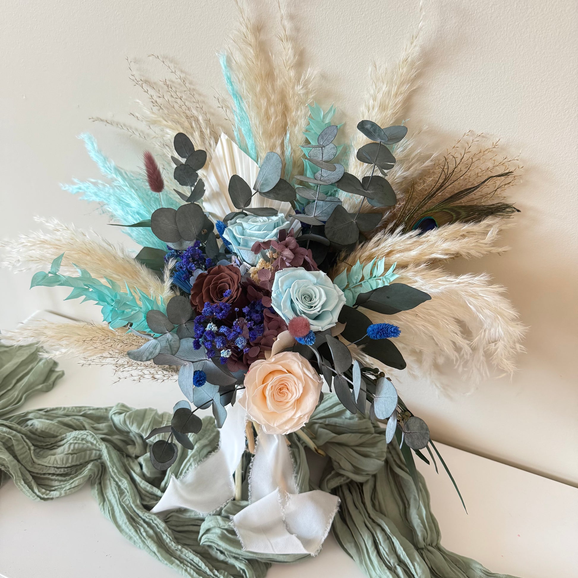 Rustic dried wedding bouquet featuring teal foliage, navy blooms and preserved grass tied with white silk ribbon.