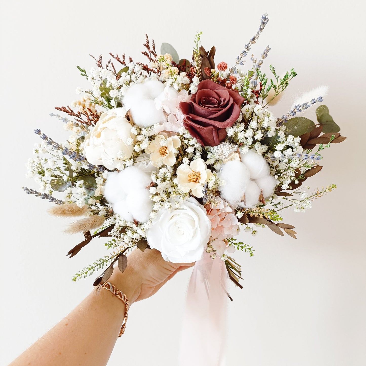 Rustic dried flower bouquet held in hand, featuring white and burgundy preserved blooms, cotton accents, and eucalyptus.