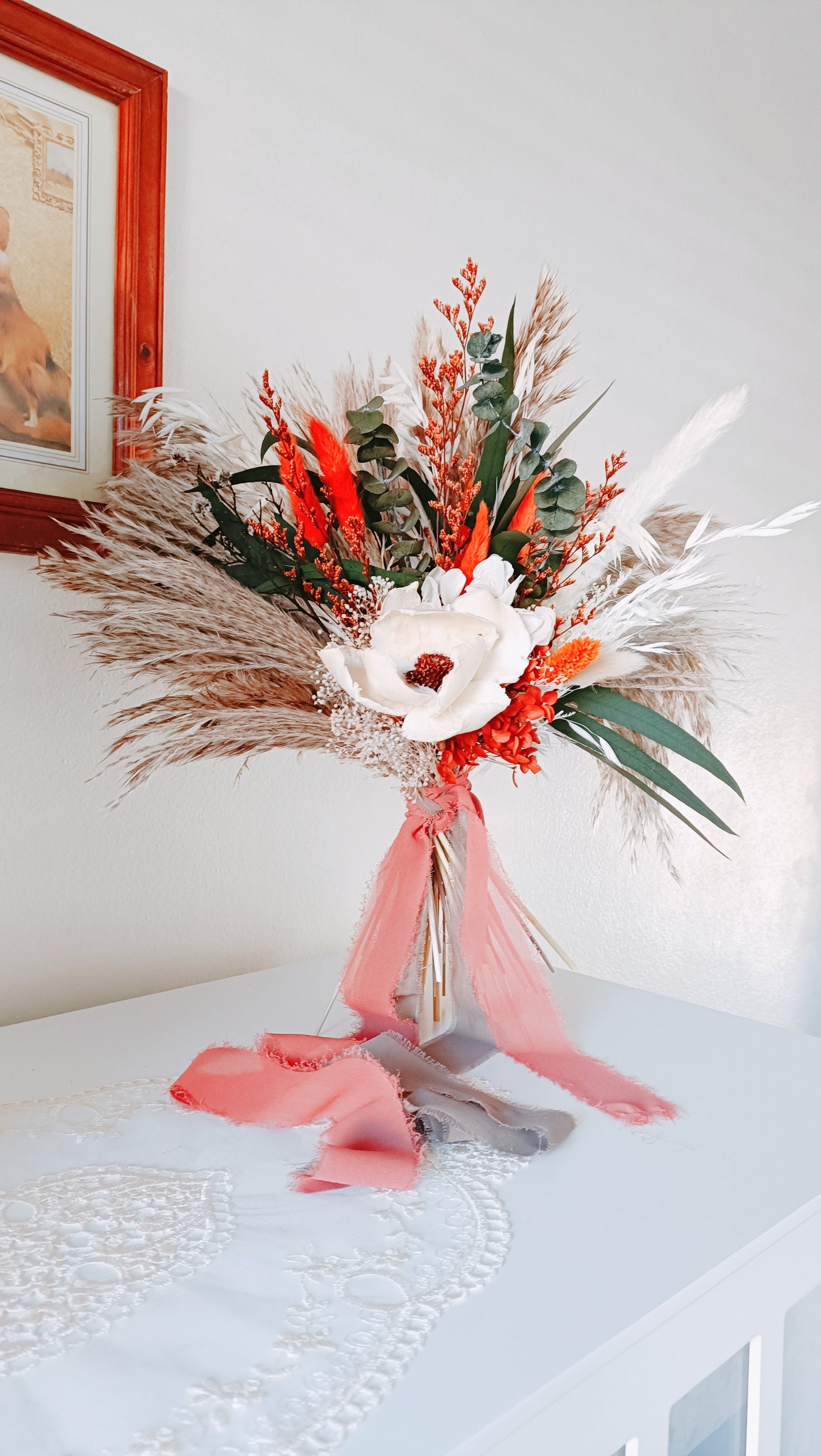 Close-up of a sola wood flower in an ivory dried bouquet, surrounded by preserved leaves and burnt orange details.