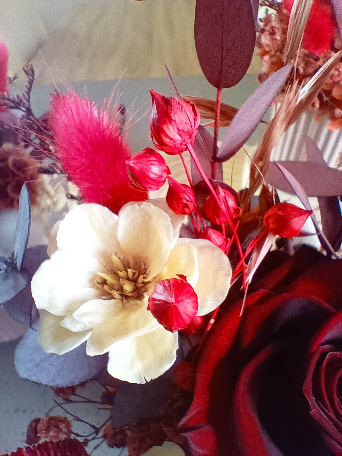 Detailed macro shot showing cream sola flowers, white cotton, red bunny tails, and surrounding textures. Emphasizes natural materials and warm romantic tones. Ideal for showcasing texture in preserved floral design.