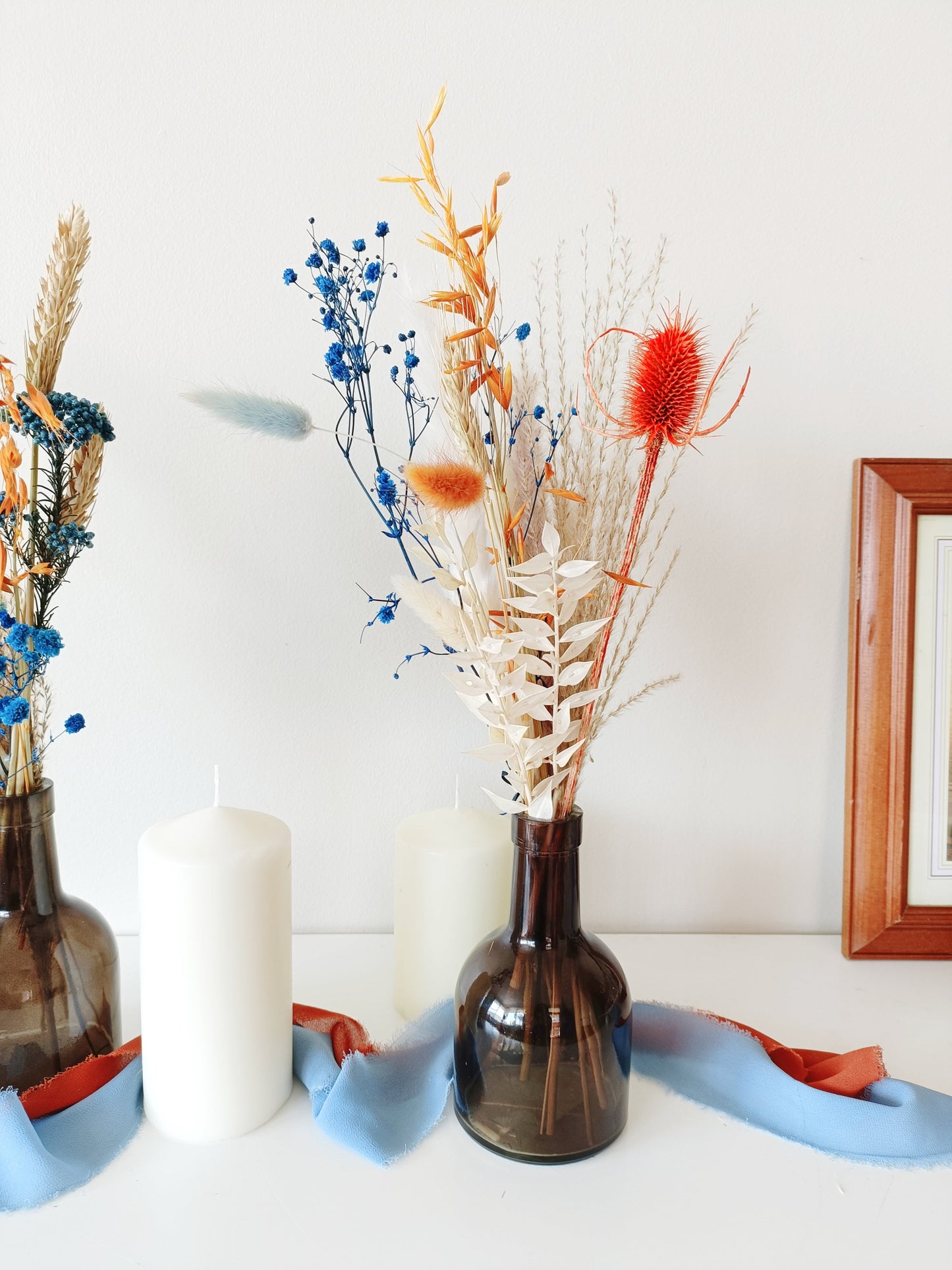 dried flower decor, vibrant floral centerpiece, blue and orange wedding flowers, artistic floral arrangement, striking dried flower setup, colorful wedding decor, preserved flower table display, unique rustic florals, dried flower boho centerpiece, modern botanical decor, vibrant boho styling, energetic floral arrangement, contrast floral table decor, wildflower-inspired setup, bright wedding flowers, dried pampas grass decor, eye-catching floral vase, handcrafted dried bouquet, colorful natural centerpiece