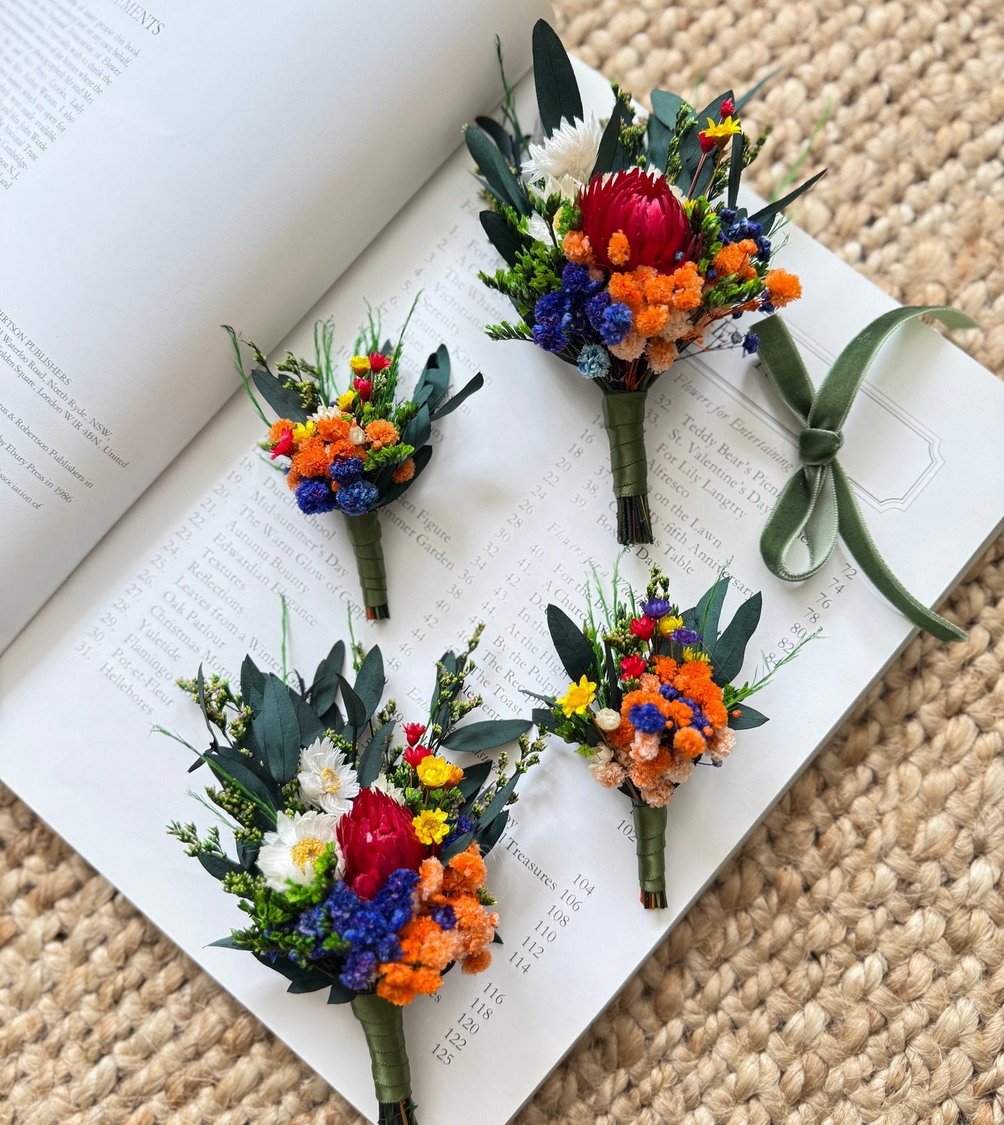 Rustic dried flower boutonniere set with burnt orange, royal blue and emerald green tones on neutral background.