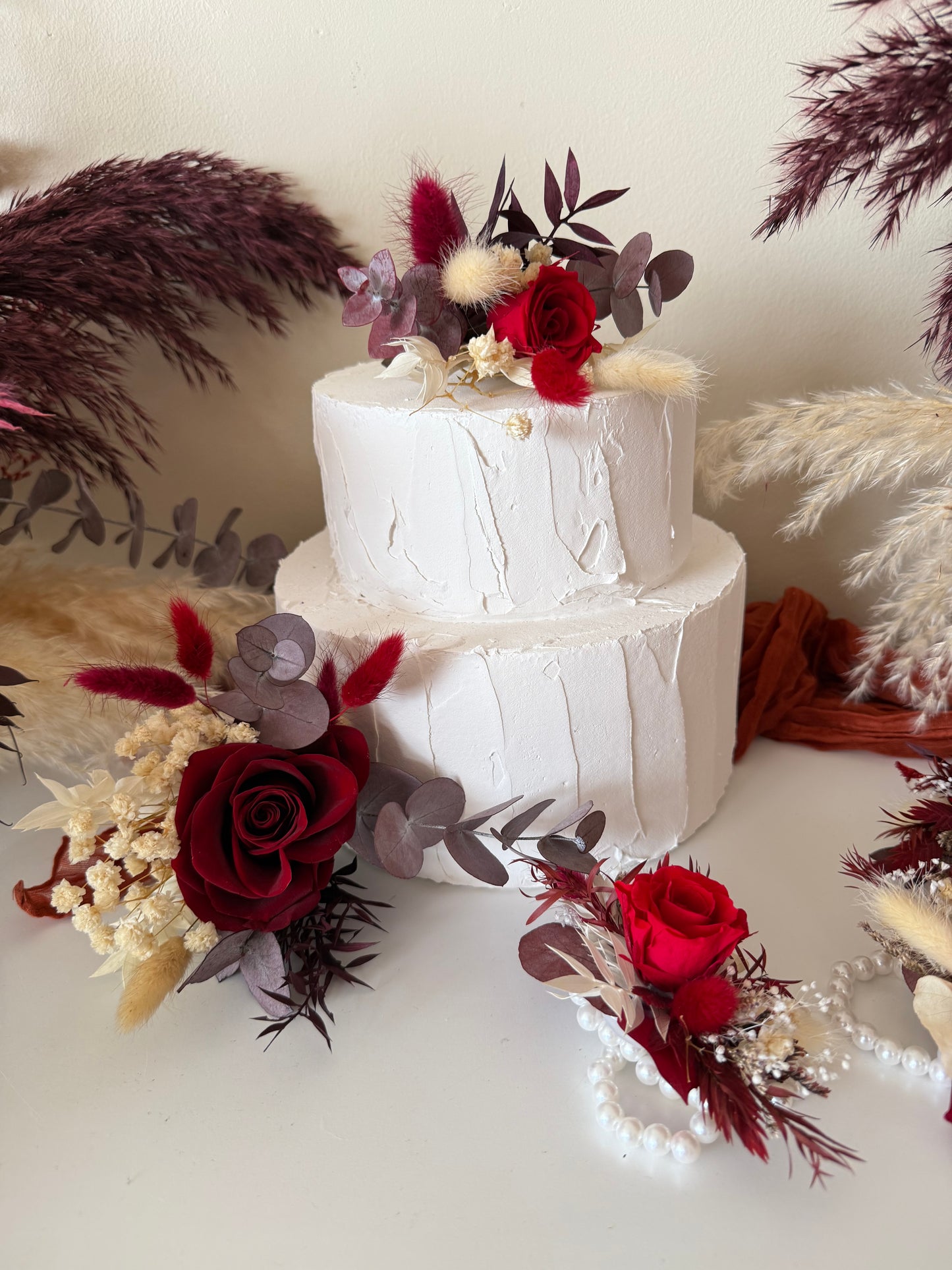 Boho-style burgundy dried flower cake topper with red ribbon and natural pampas background