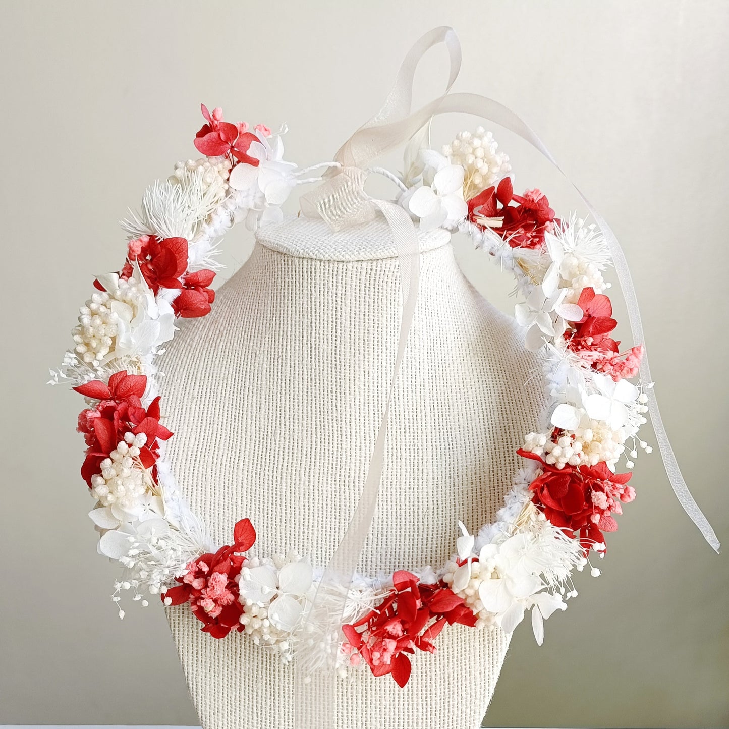 A delicate dried flower crown featuring a bold mix of red and white petals, adorned with tiny pearl accents. The wreath is tied with sheer ribbon, creating an elegant, romantic look for a wedding or special occasion.