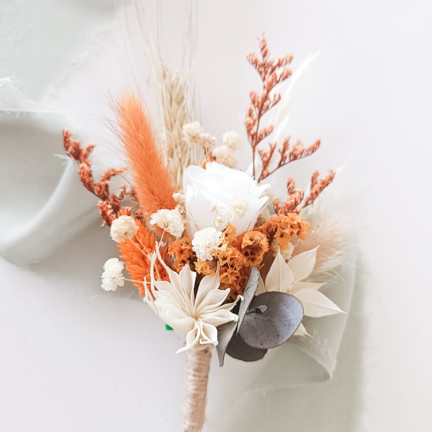 Compact preserved flower arrangement in bright orange and ivory tones, combining sola roses, eucalyptus, bunny tails and wheatgrass.