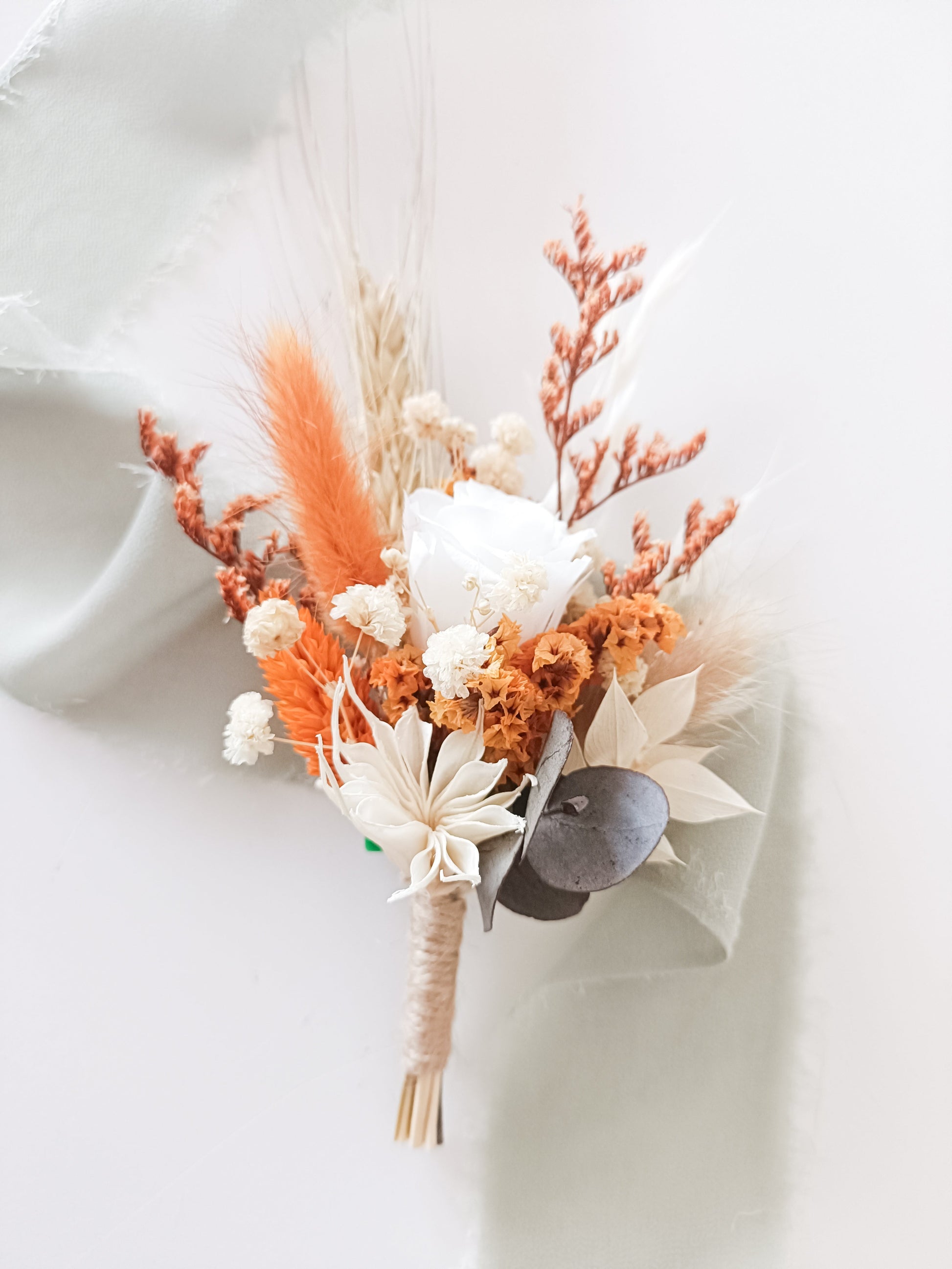 Compact preserved flower arrangement in bright orange and ivory tones, combining sola roses, eucalyptus, bunny tails and wheatgrass.