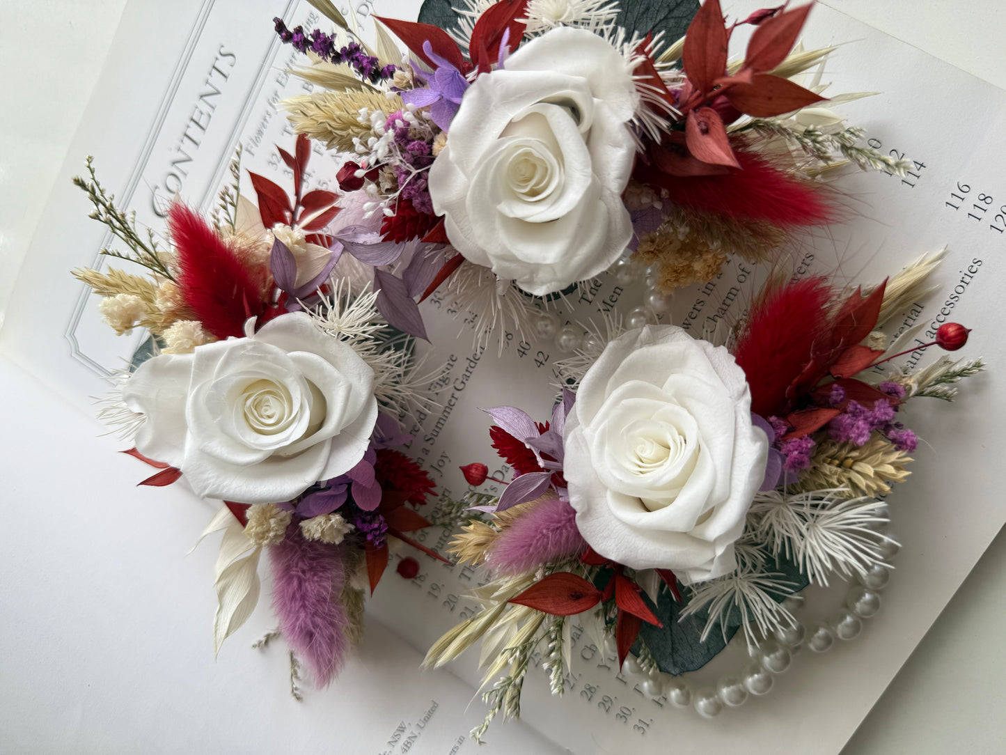 Three white flower corsages with red and purple accents on an open book