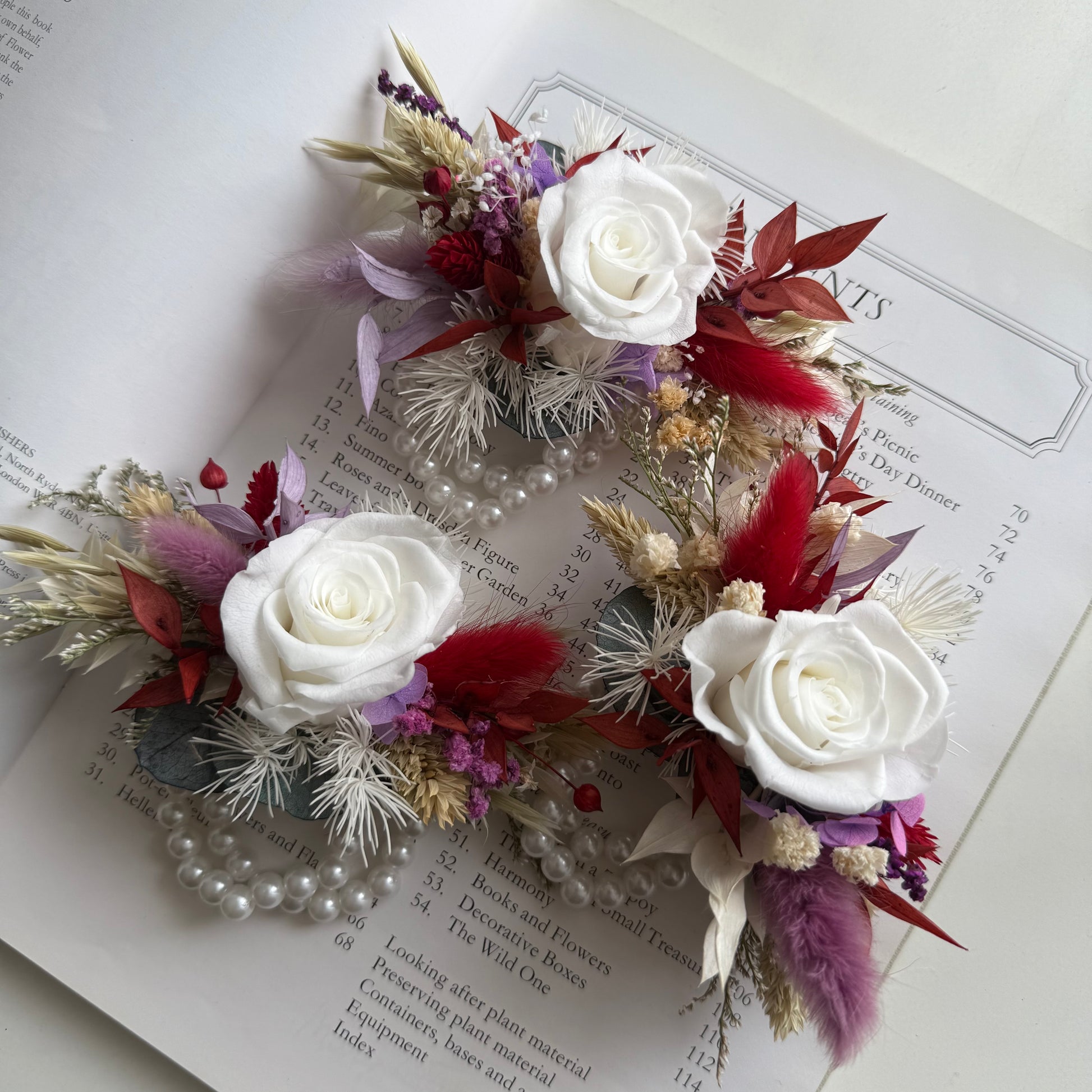 Floral corsages with white roses and red and purple accents on an open book