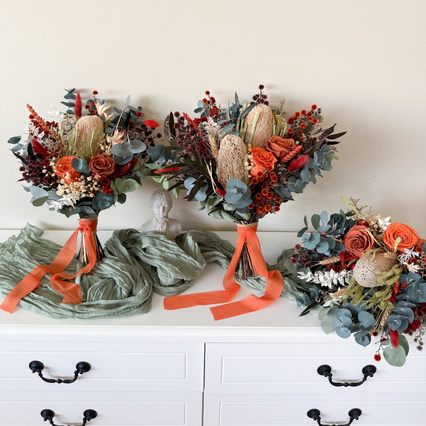 Three floral arrangements with orange ribbons on a white surface.