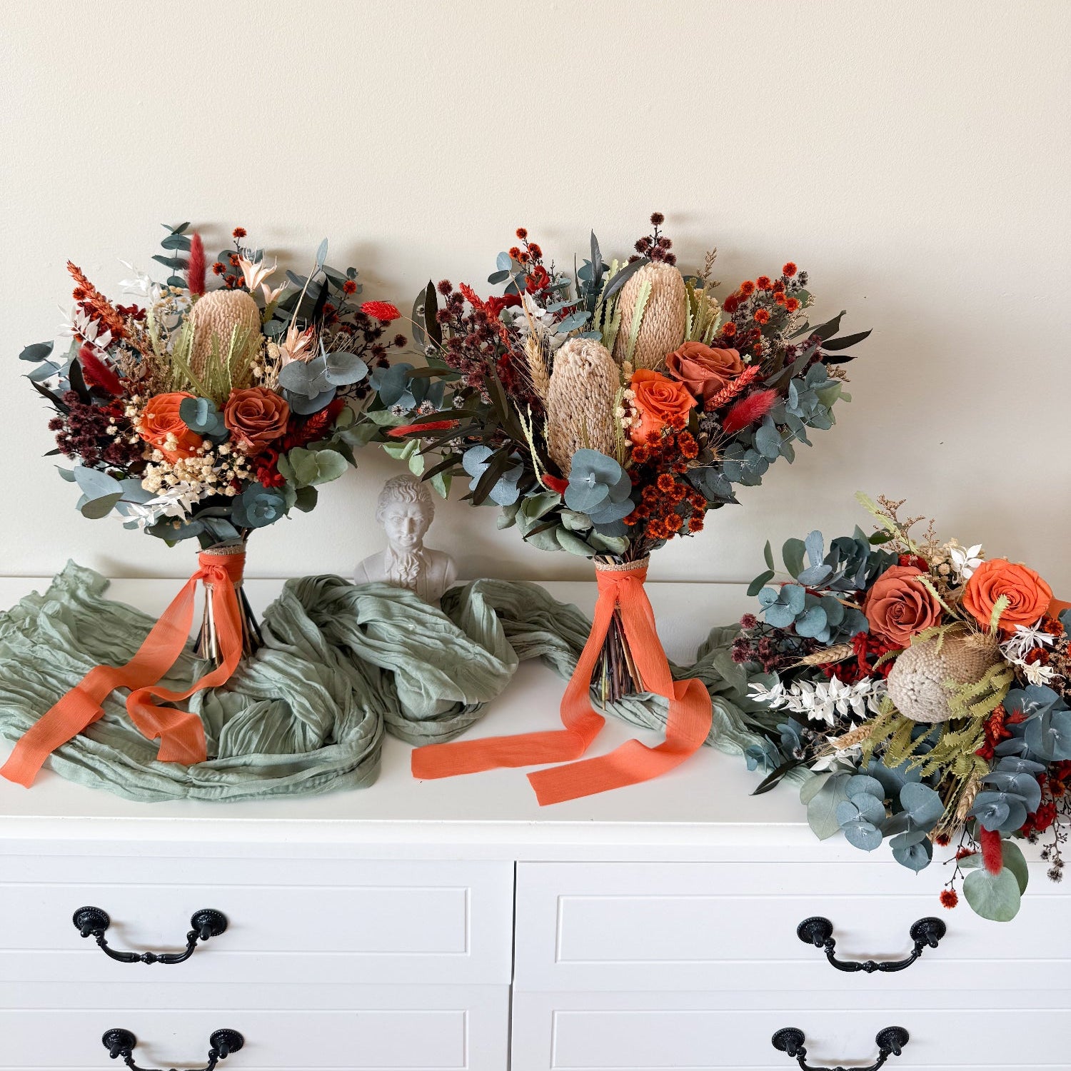 Three floral arrangements with orange ribbons on a white surface.