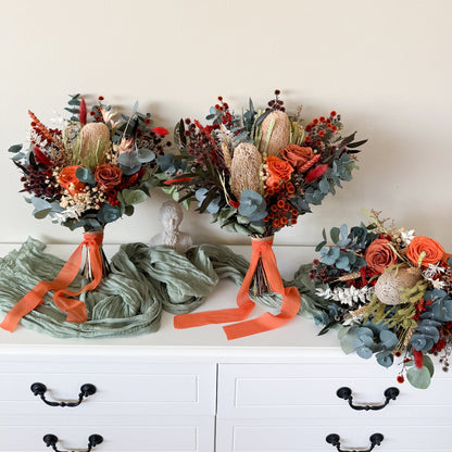 Three floral arrangements with orange ribbons on a white surface.