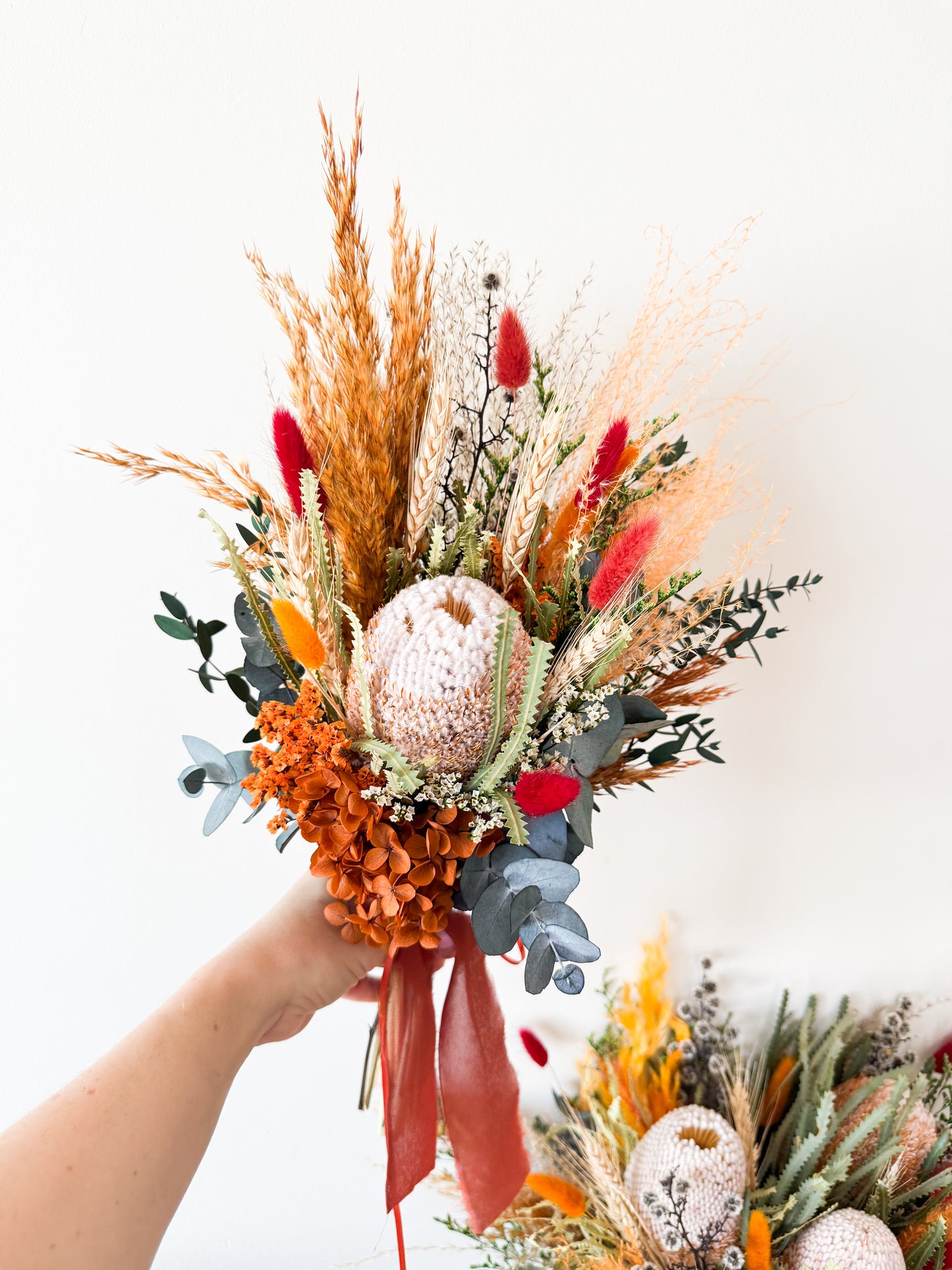Bouquet of dried flowers with a hand holding it against a white background