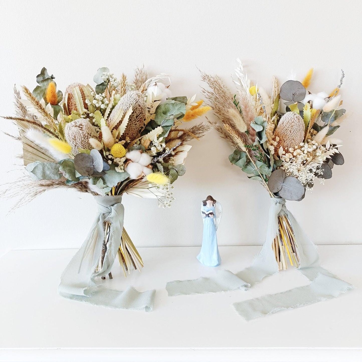 Neutral-toned wedding bouquet featuring dried banksia, yellow billy buttons, eucalyptus, and cotton â€“ hand-tied and wrapped in a soft sage ribbon.