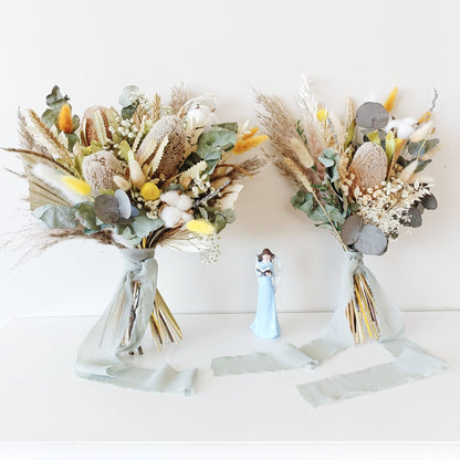 Neutral-toned wedding bouquet featuring dried banksia, yellow billy buttons, eucalyptus, and cotton â€“ hand-tied and wrapped in a soft sage ribbon.