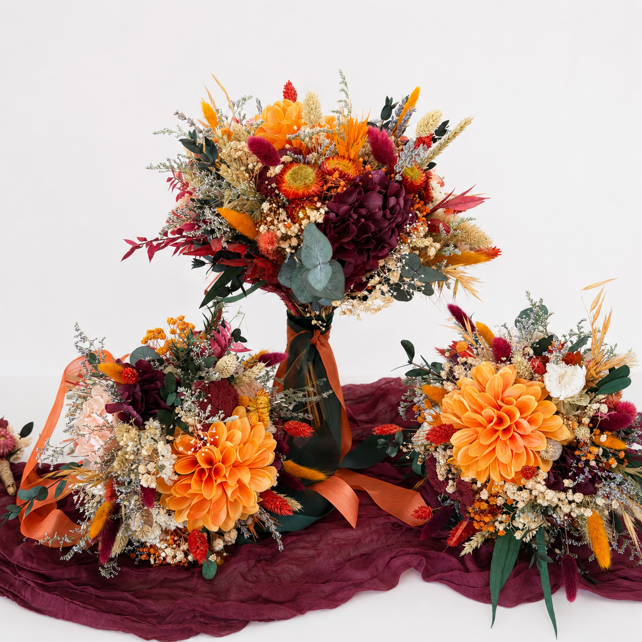 Autumn burnt orange and burgundy dried flower wedding collection including bridal bouquet, two bridesmaid bouquets and matching boutonnières.