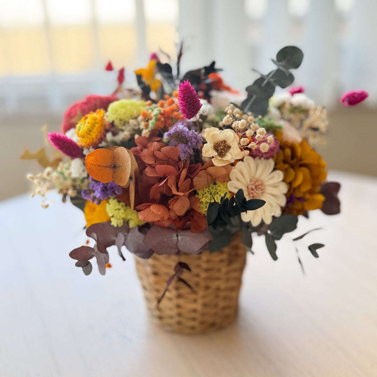 Colorful flower arrangement in a woven basket on a light surface with a blurred background