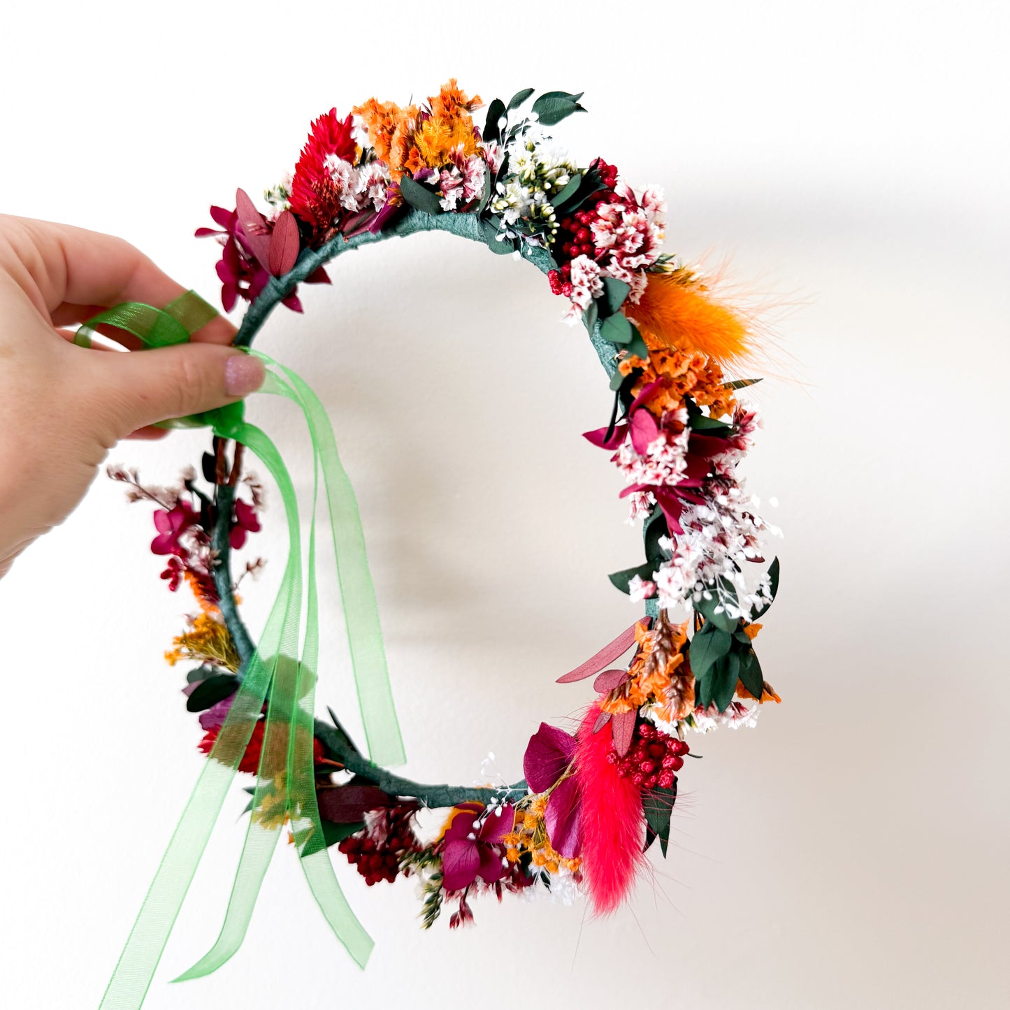Autumn flower crown resting on a wooden picture frame, showing preserved flowers in fall colours and a trailing green ribbon.