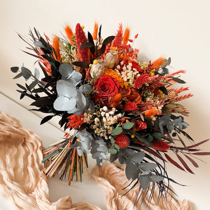 Autumnal flower arrangement with red, orange, and black flowers on a white surface