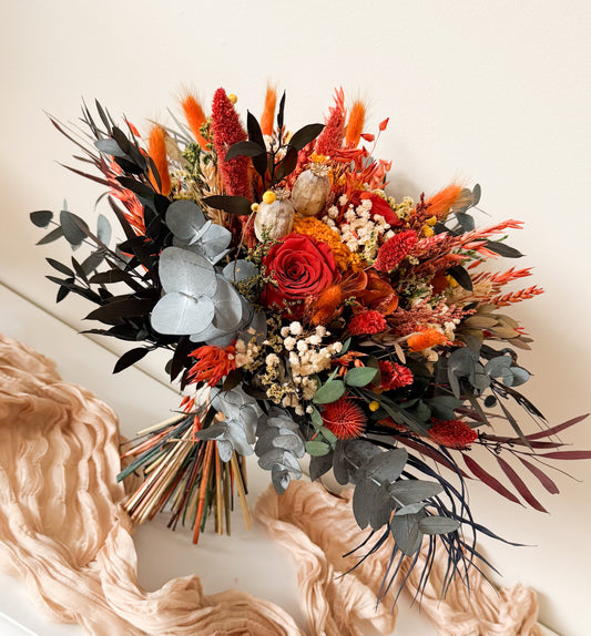 Autumnal flower arrangement with red, orange, and black flowers on a white surface.