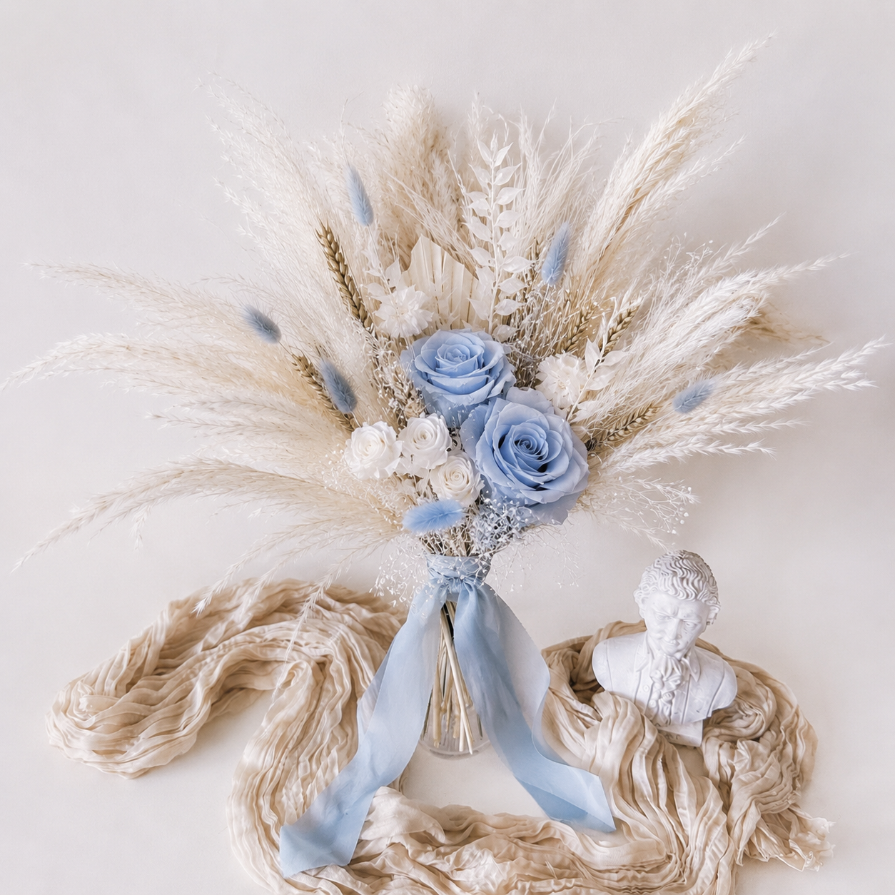 dried bridal bouquett with blue flowers, pampas grass, and a bust on a light background