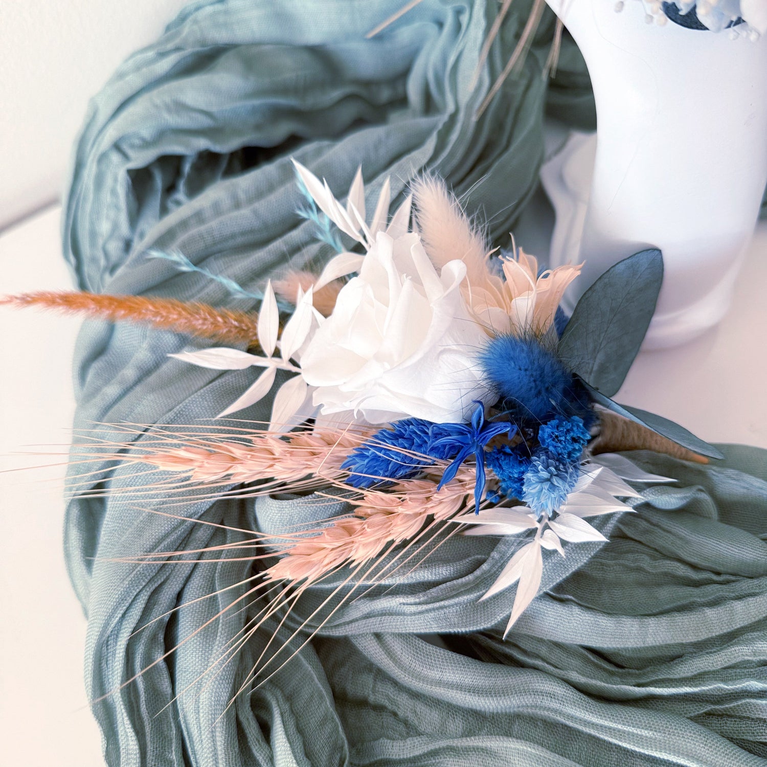 Close-up of two dried boutonnieres in soft blue and ivory tones, tied with jute twine, handmade for rustic weddings.