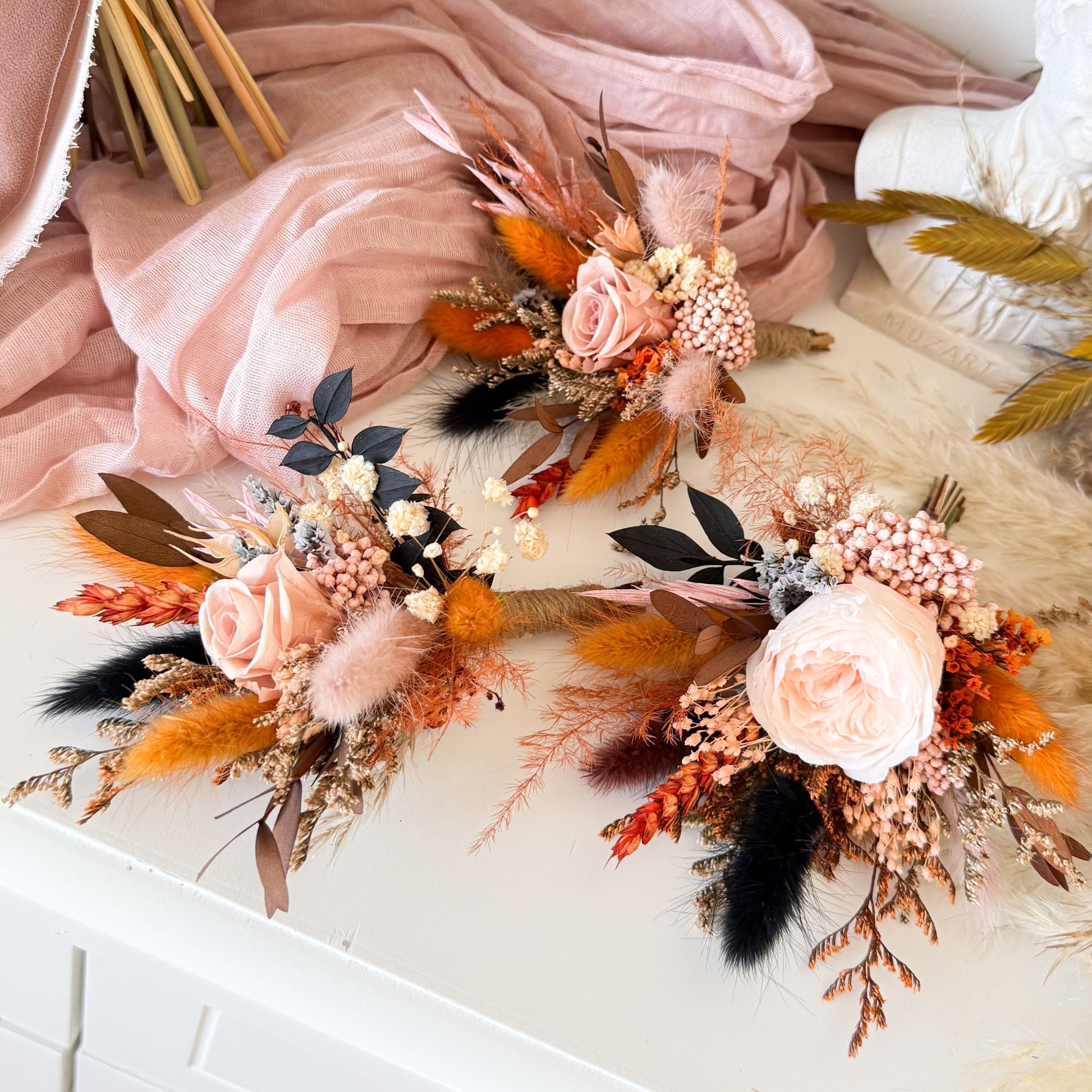 Blush and terracotta dried flower boutonnieres arranged on white dresser.