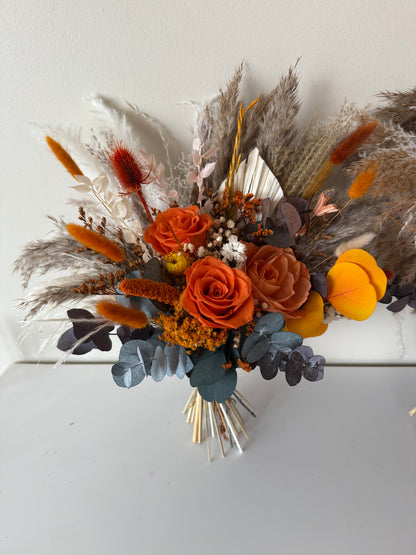 Back view of a dried wedding bouquet with visible stems, featuring terracotta and yellow preserved flowers, eucalyptus leaves, and pampas grass.